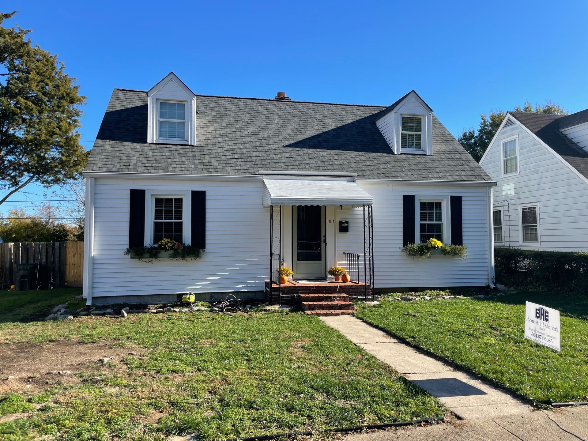White house with gray roof and black shutters, front walkway, porch, and small lawn under a clear blue sky