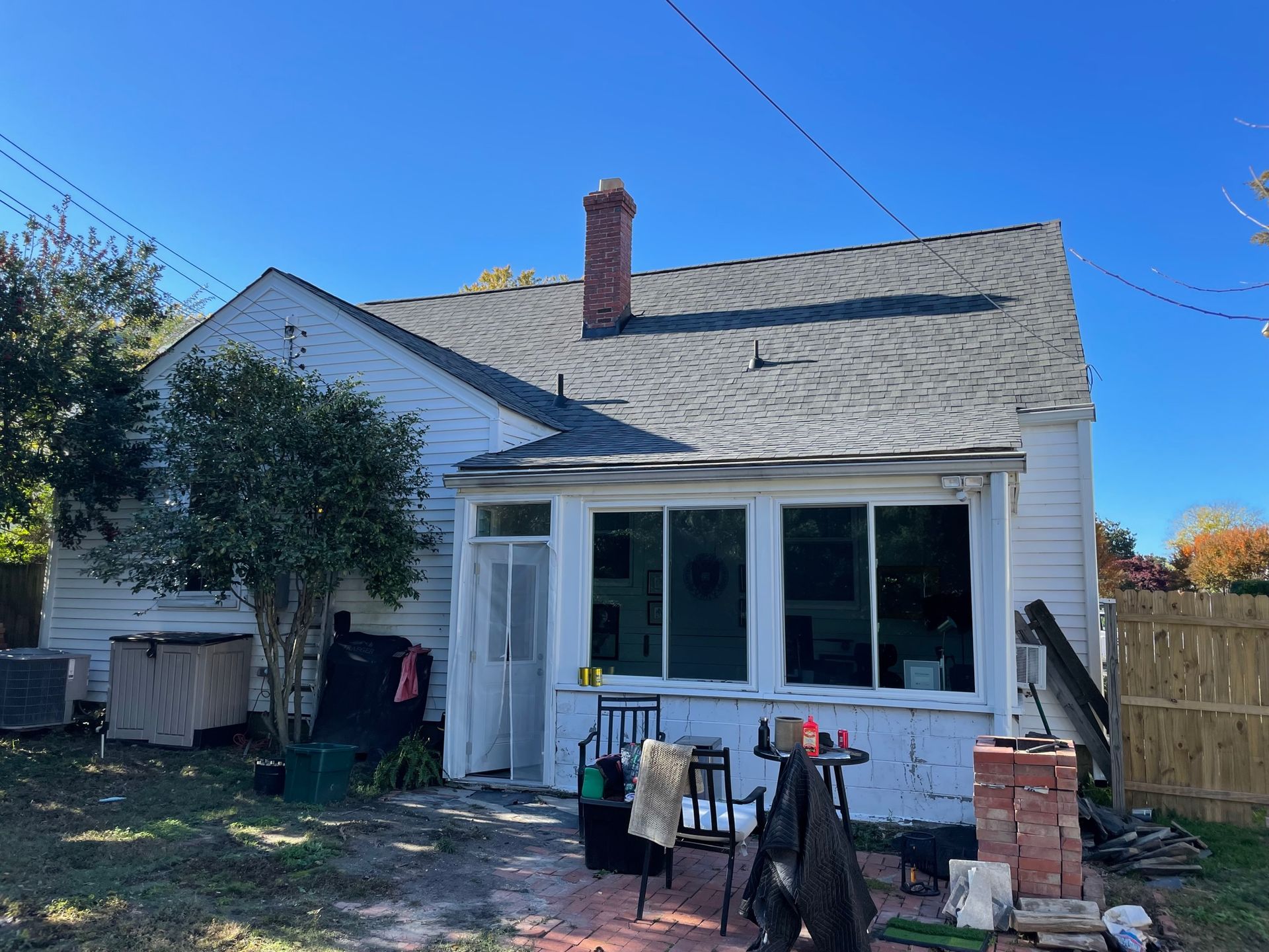 Small white house with a chimney and front porch, tools and supplies outside under a clear blue sky