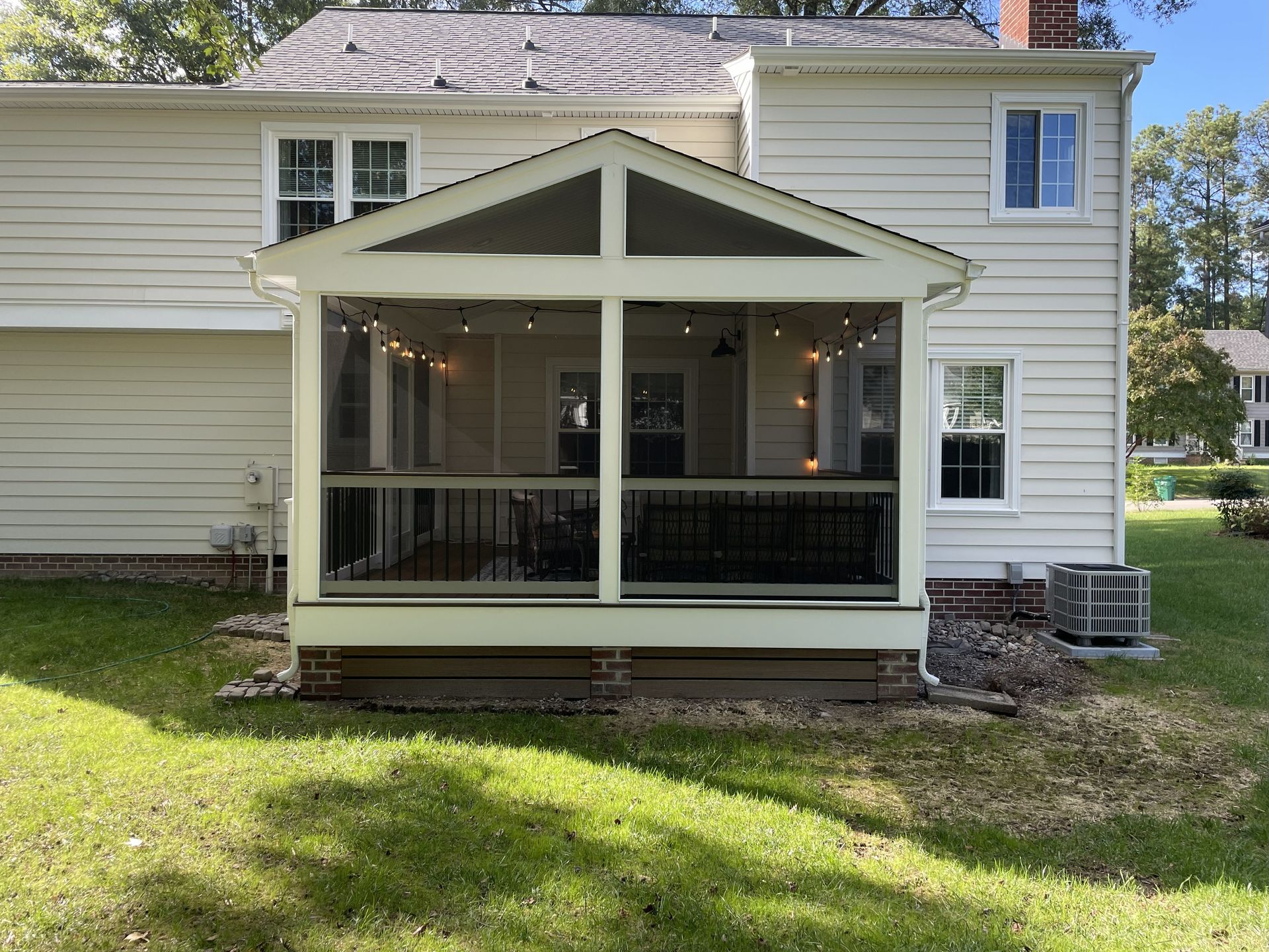 Front porch with screened enclosure on a beige house, black railing, and lawn in front