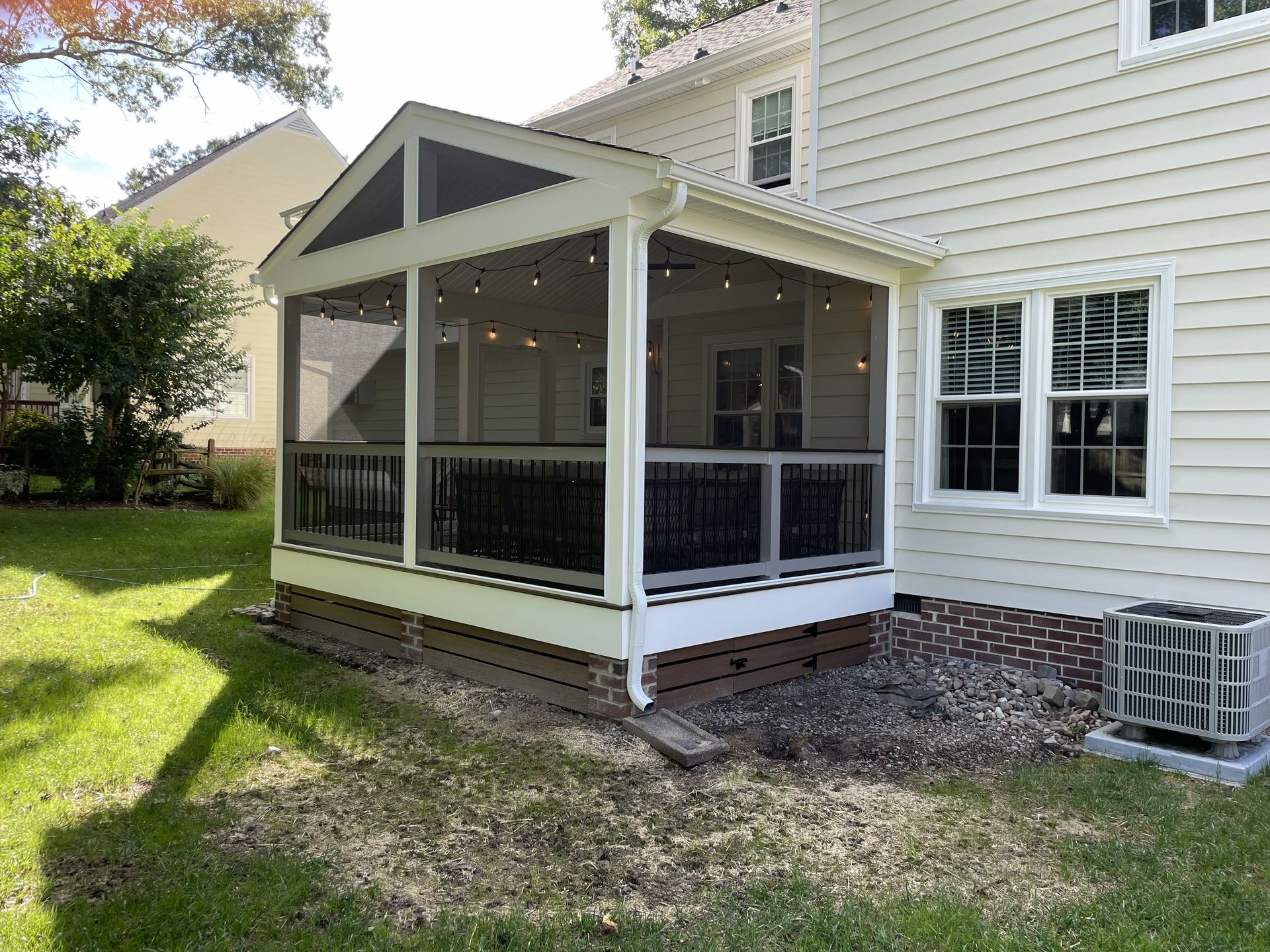 Screened-in porch on a white house with black railings and a small deck in a grassy backyard