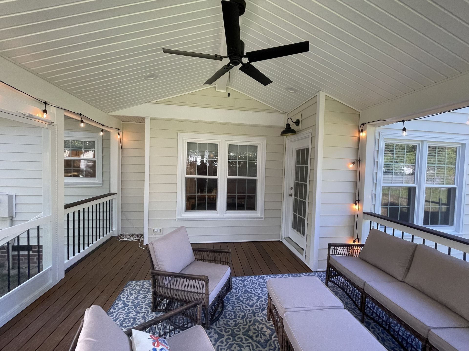 Covered porch with ceiling fan, string lights, and wicker seating with cushions and rug.