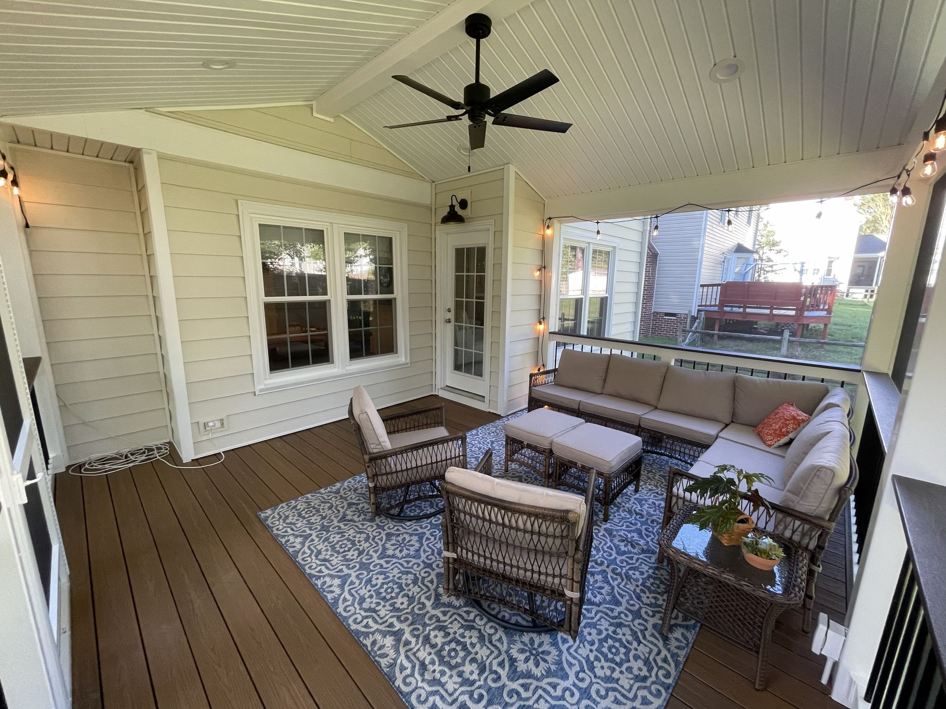 Covered porch with wicker seating, patterned rug, ceiling fan, and white siding.