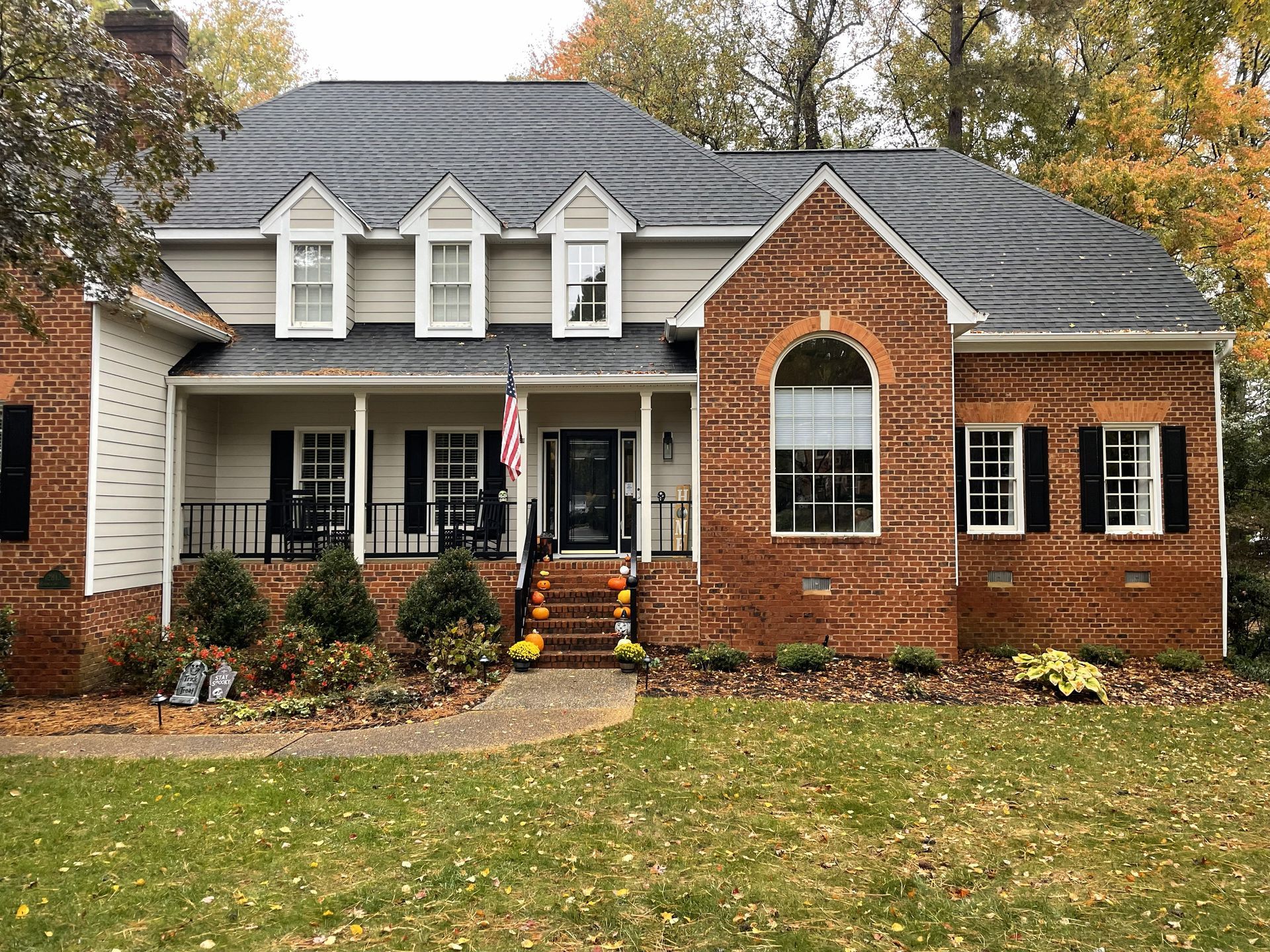 Brick suburban house with white trim, front porch, and autumn trees in the yard