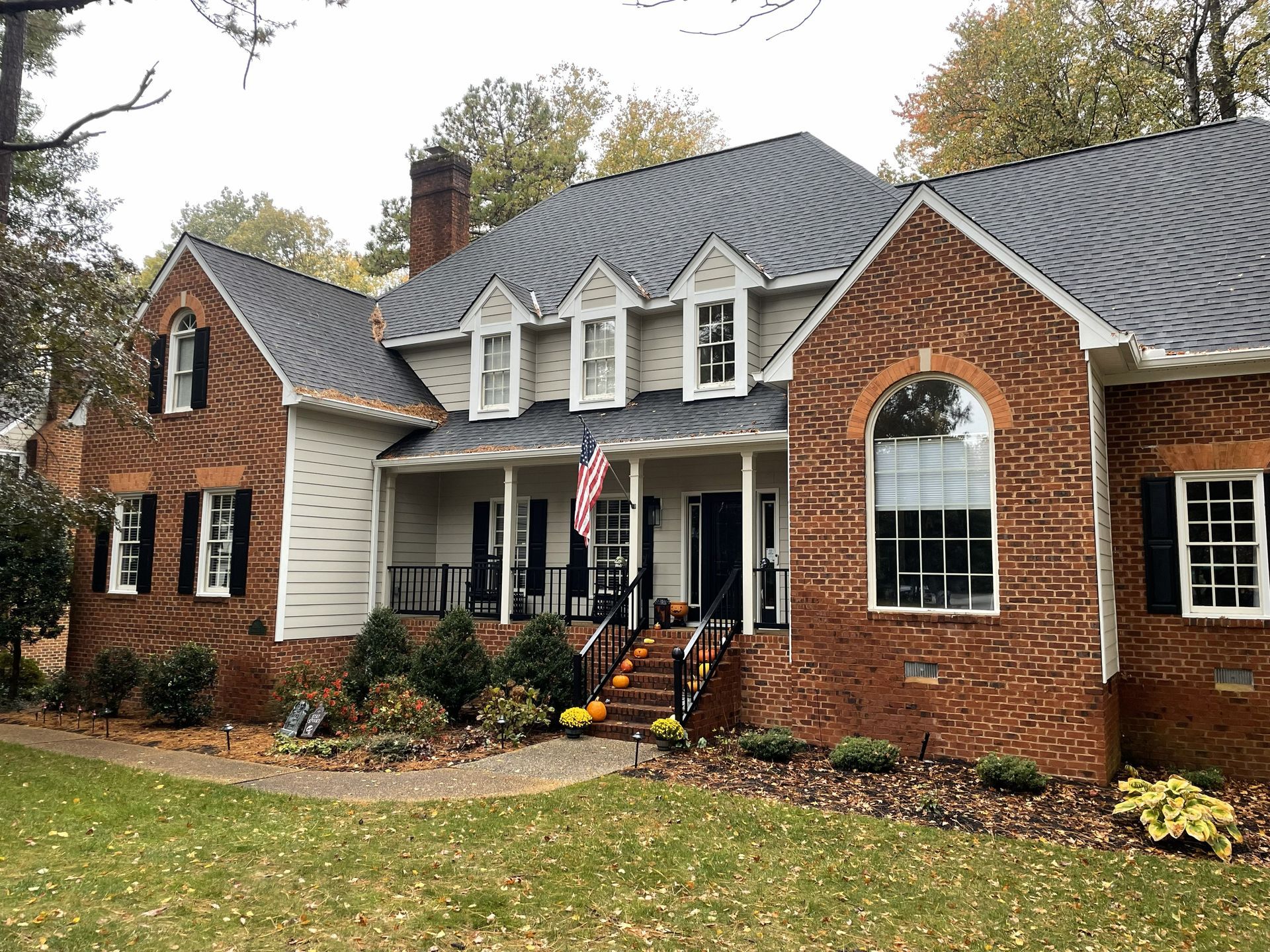 Large brick suburban house with white trim, covered porch, and autumn landscaping under a gray roof