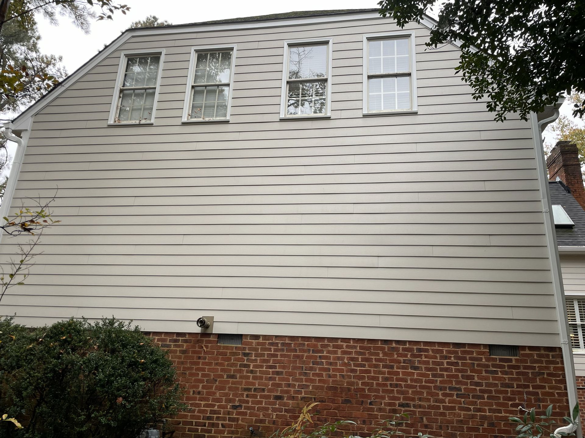 Side of a white house with horizontal siding above a brick foundation and several windows under a cloudy sky