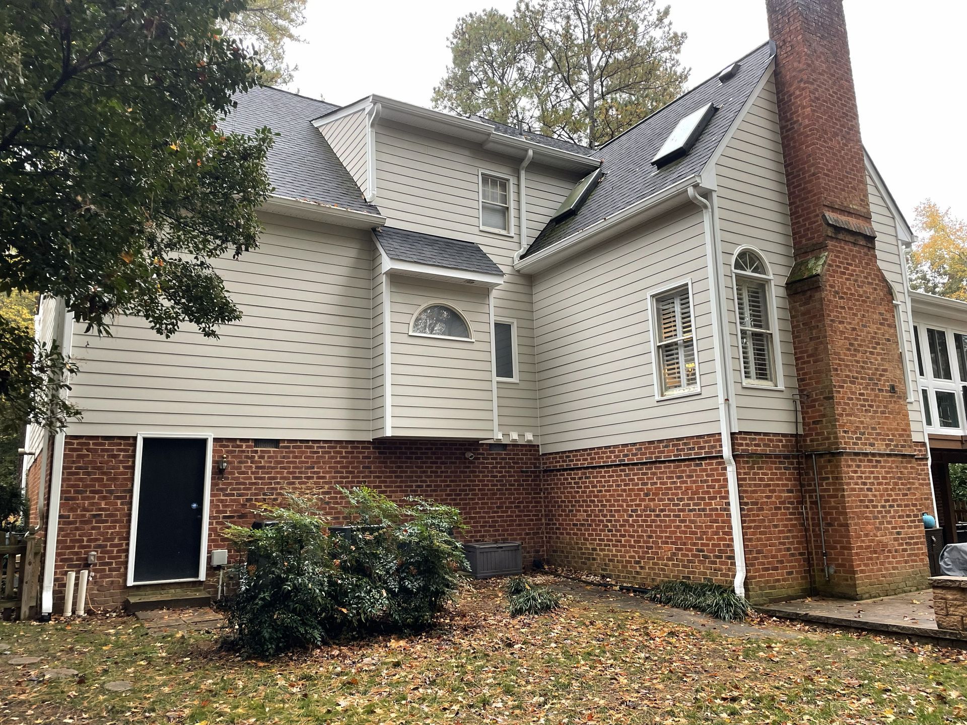 Two-story house with white siding, red brick, chimney, and a small front yard with bushes.