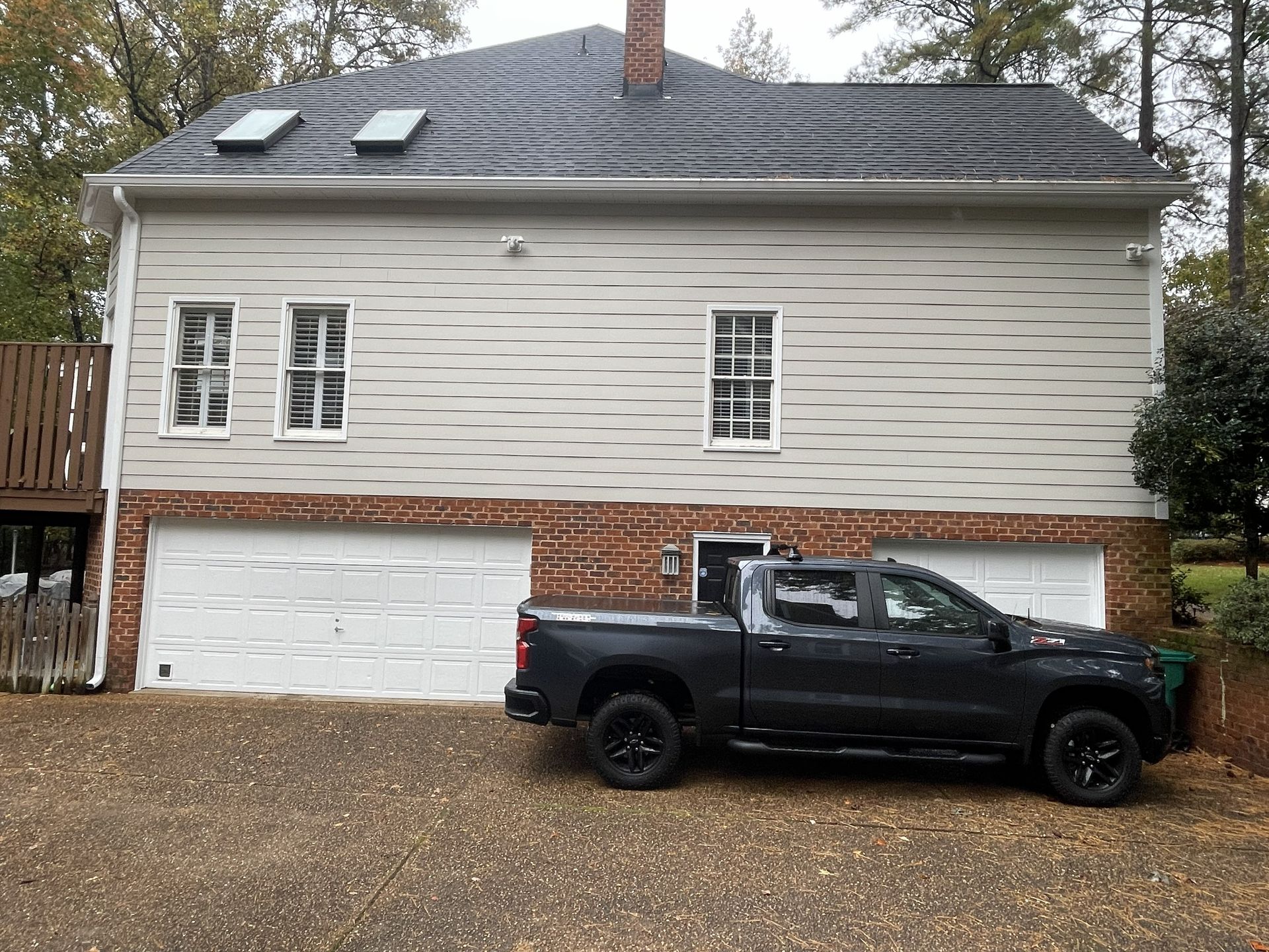 Black pickup truck parked in front of a beige house with a white garage door and brick lower facade
