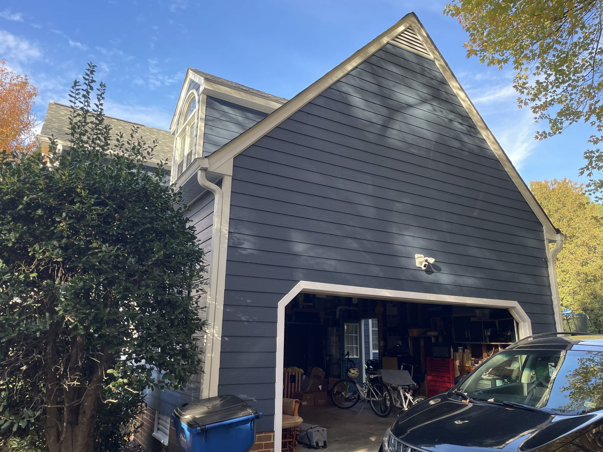 Gray house with an open garage, driveway, and trees under a blue sky