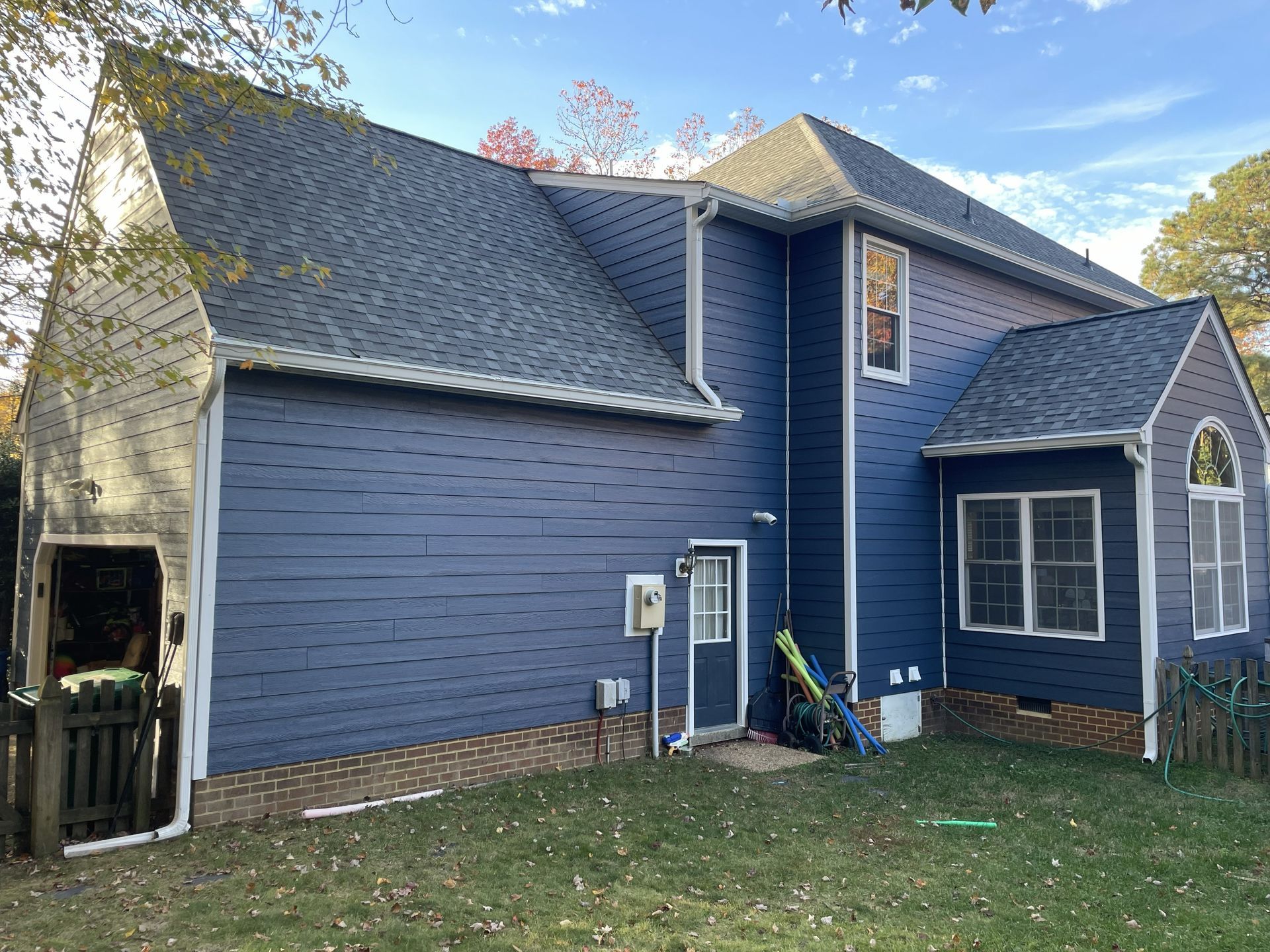 Blue two-story house with gray roof and brick foundation, viewed from the backyard.