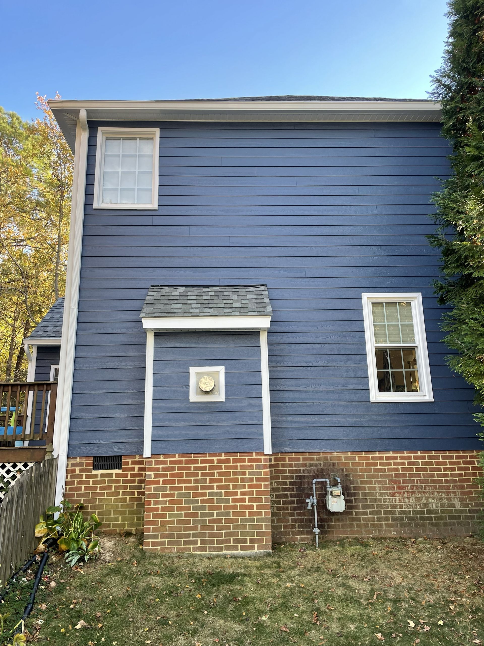 Blue two-story house with brick foundation and small windows, viewed from the backyard.