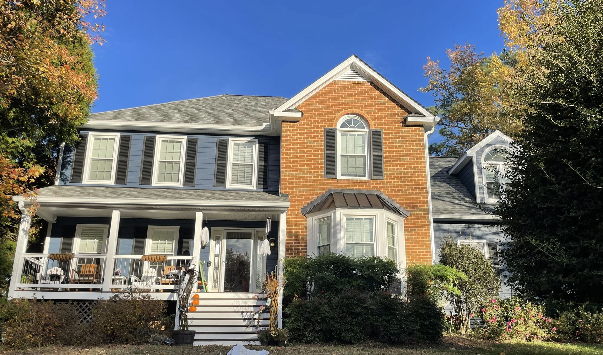 Two-story brick house with a front porch, white trim, and autumn trees in the yard.