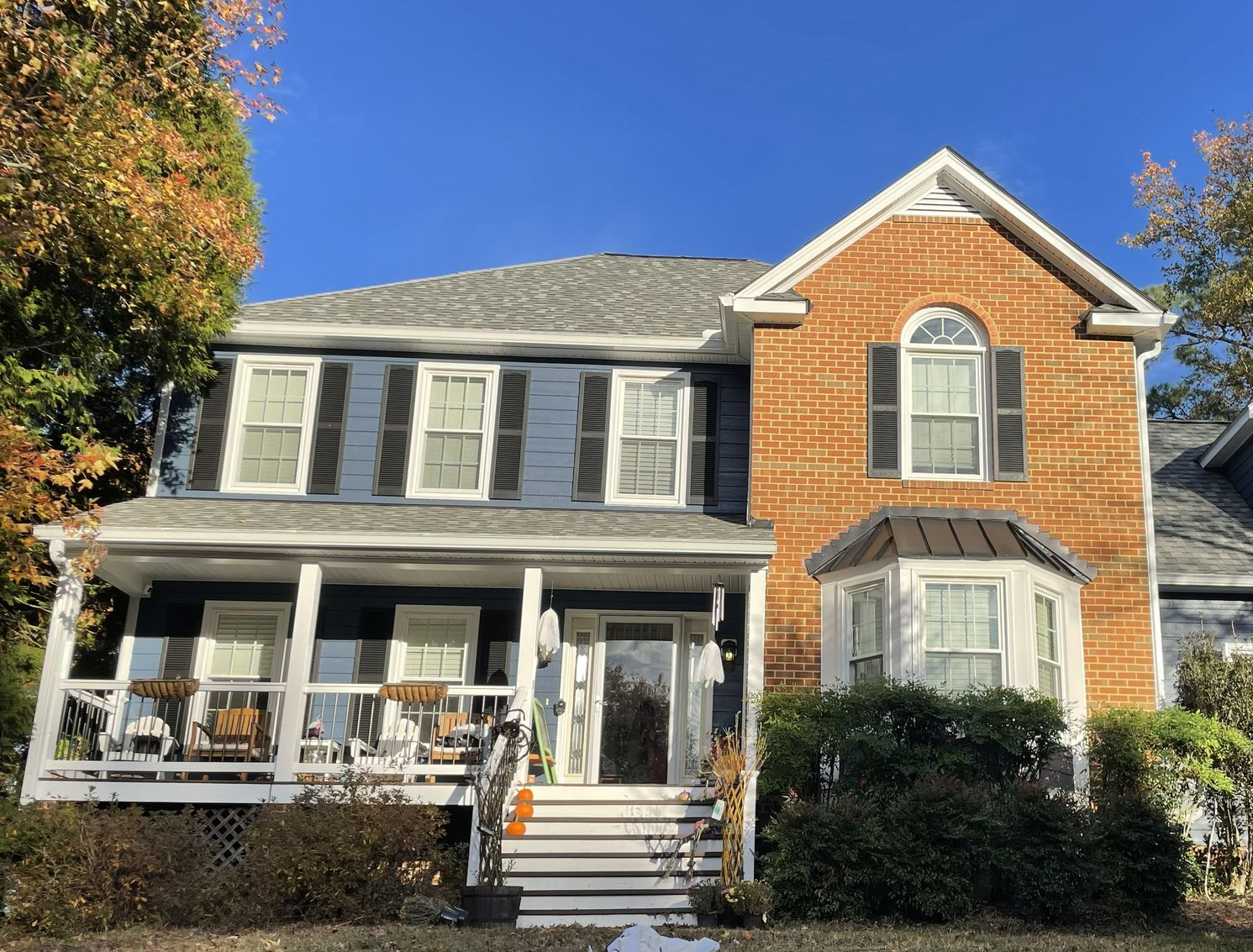 Two-story gray and brick house with white porch and steps under a blue sky