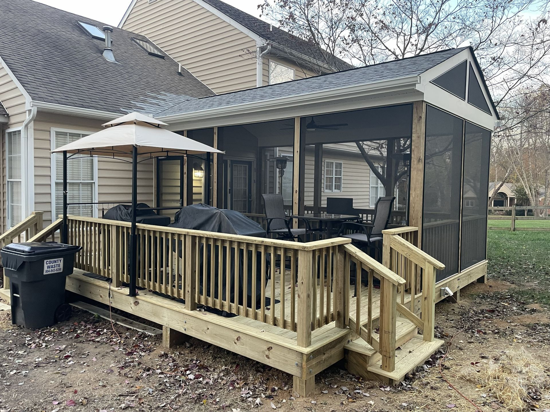 Wooden backyard deck with gazebo, steps, and railing beside a house in a fenced yard