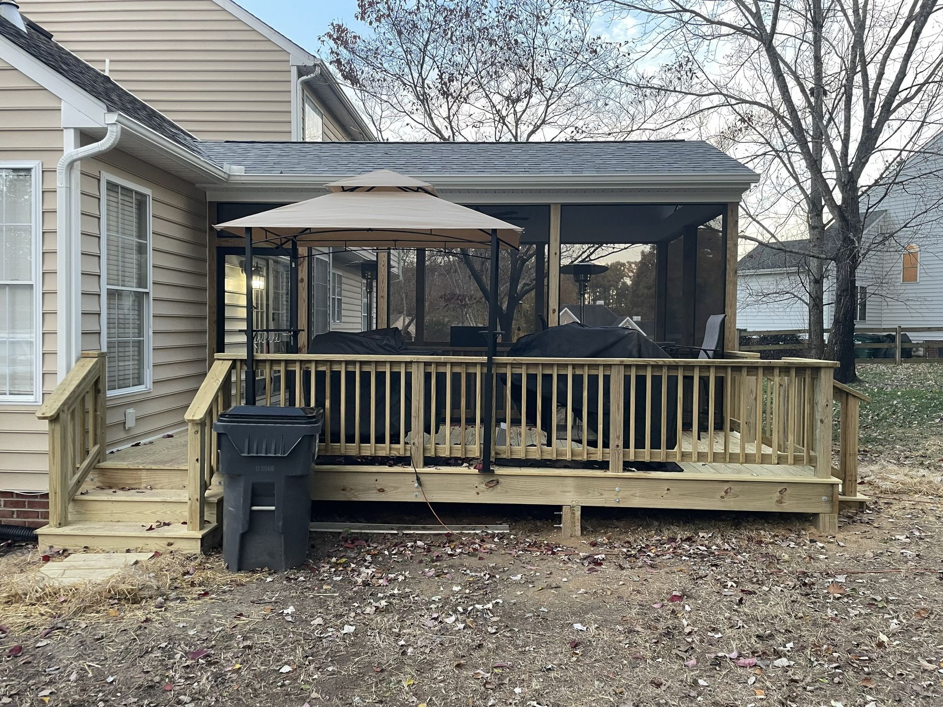 Backyard deck with wooden railing, covered patio, grill, and beige house siding