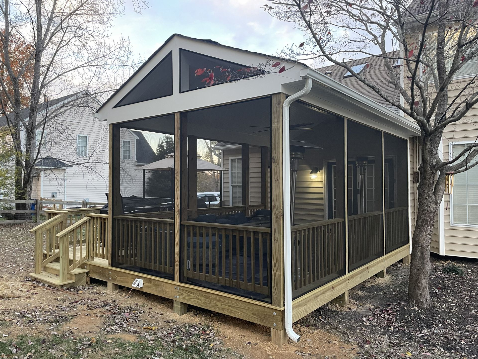 Small screened porch with dark trim, wood steps, and a gabled roof in a backyard.
