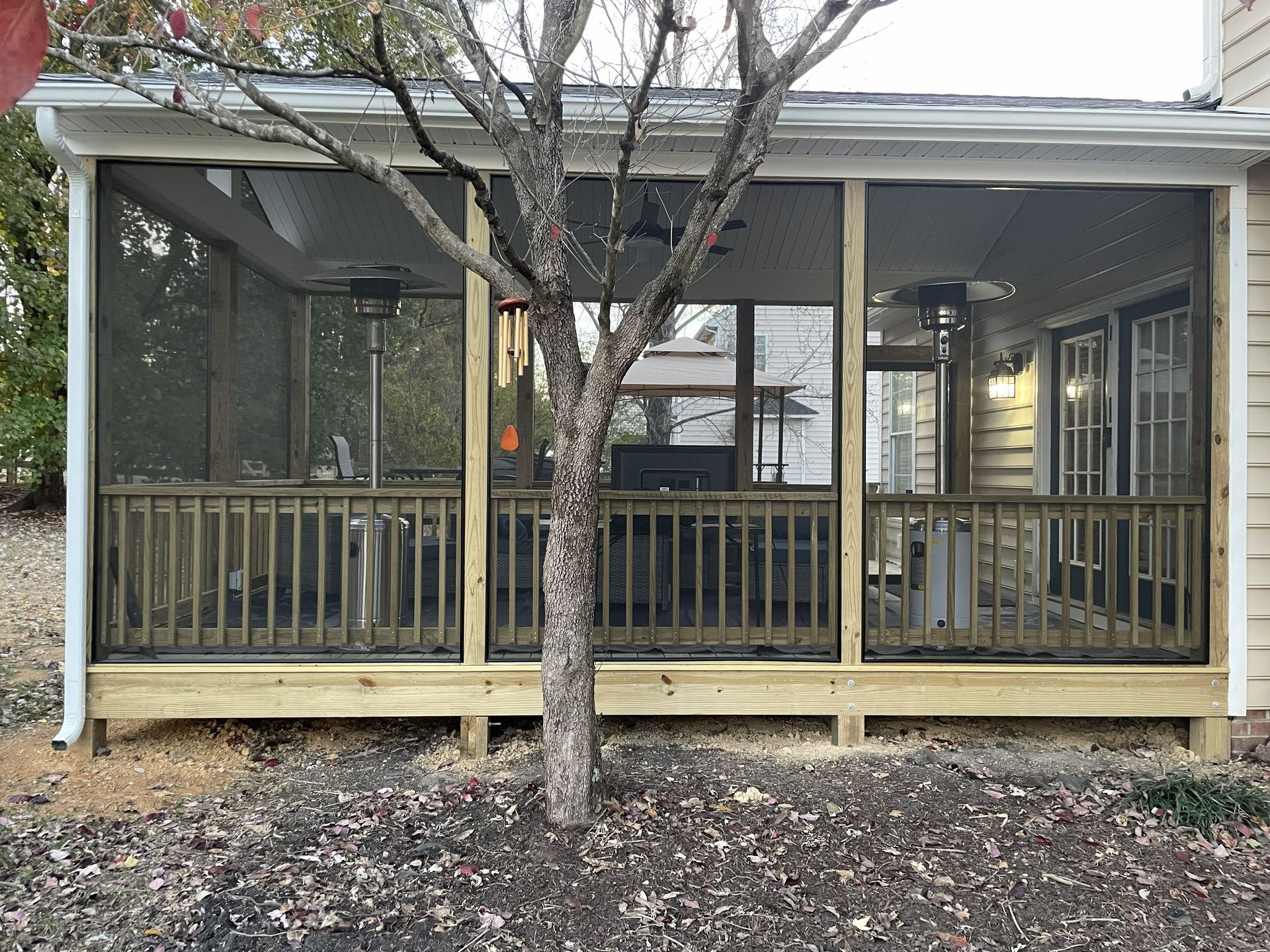 Front porch with screened windows, wooden railing, and a tree in front of a house.