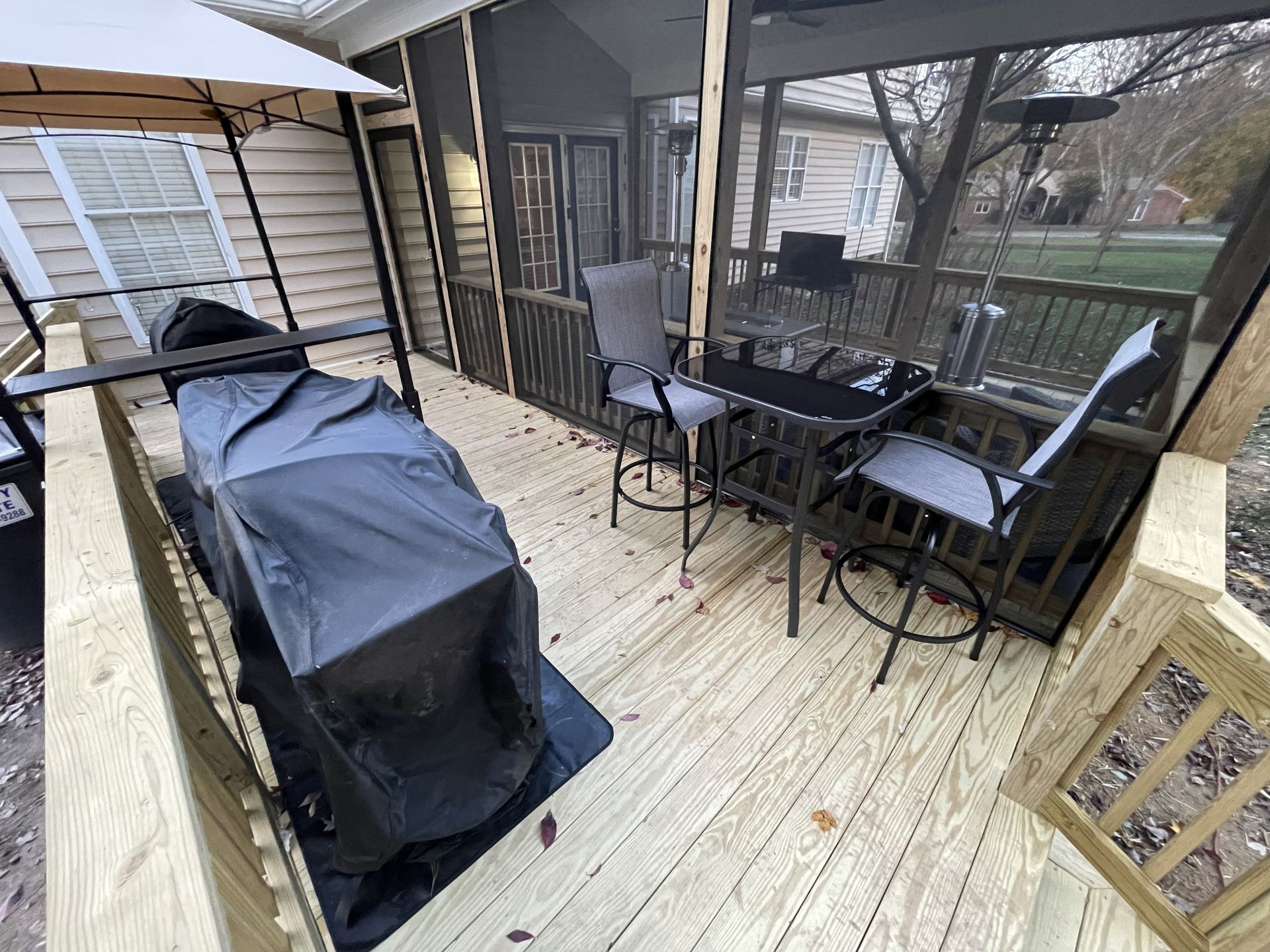 Covered patio with grill, table and chairs on a wooden deck overlooking a yard