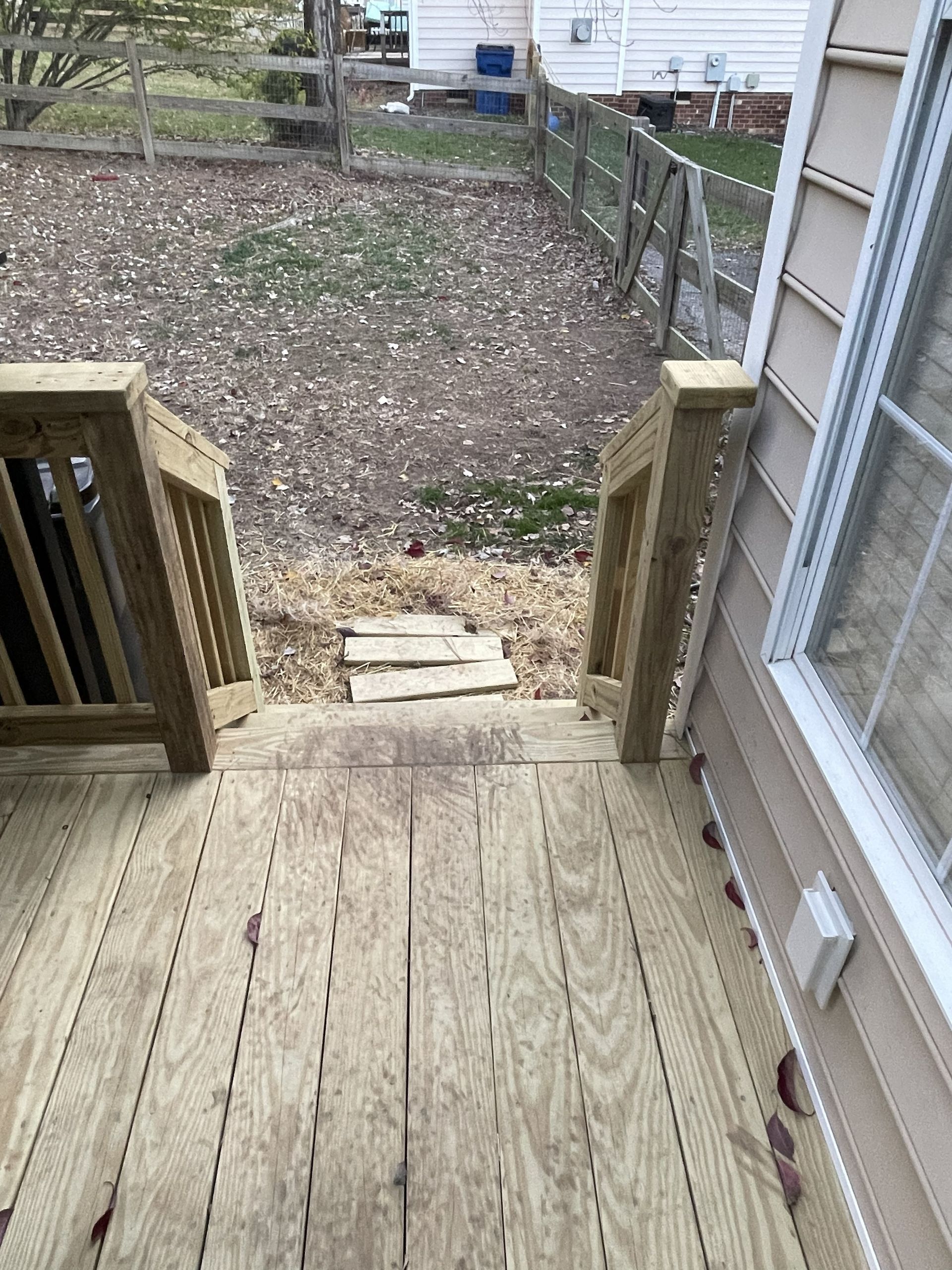 Wooden deck steps leading to a fenced backyard with gravel and a white shed