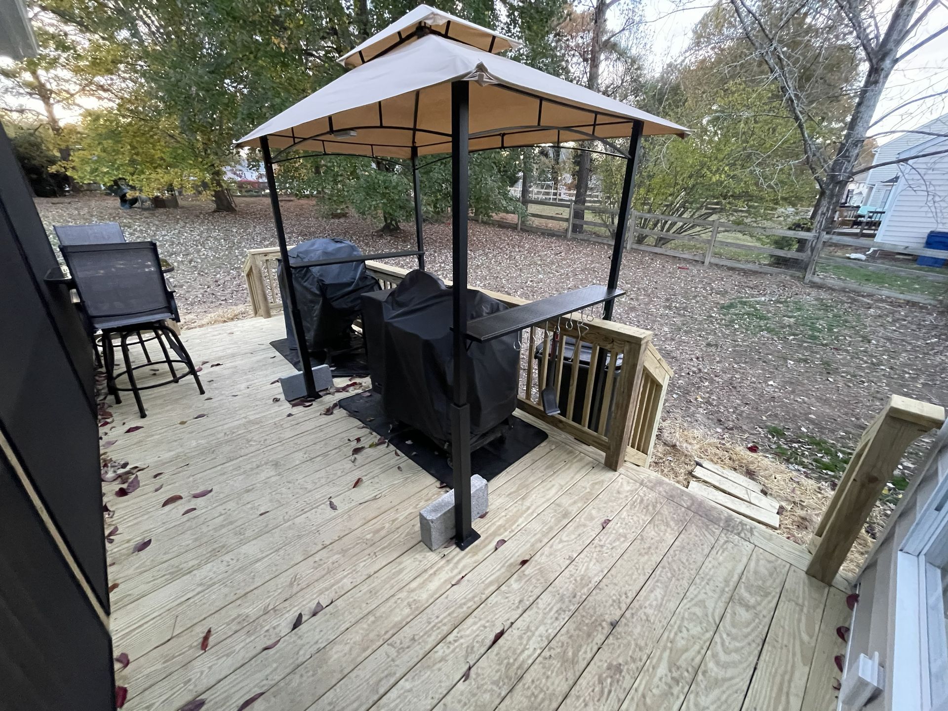 Backyard deck with covered patio seating, black grill, and wooden stairs in fall