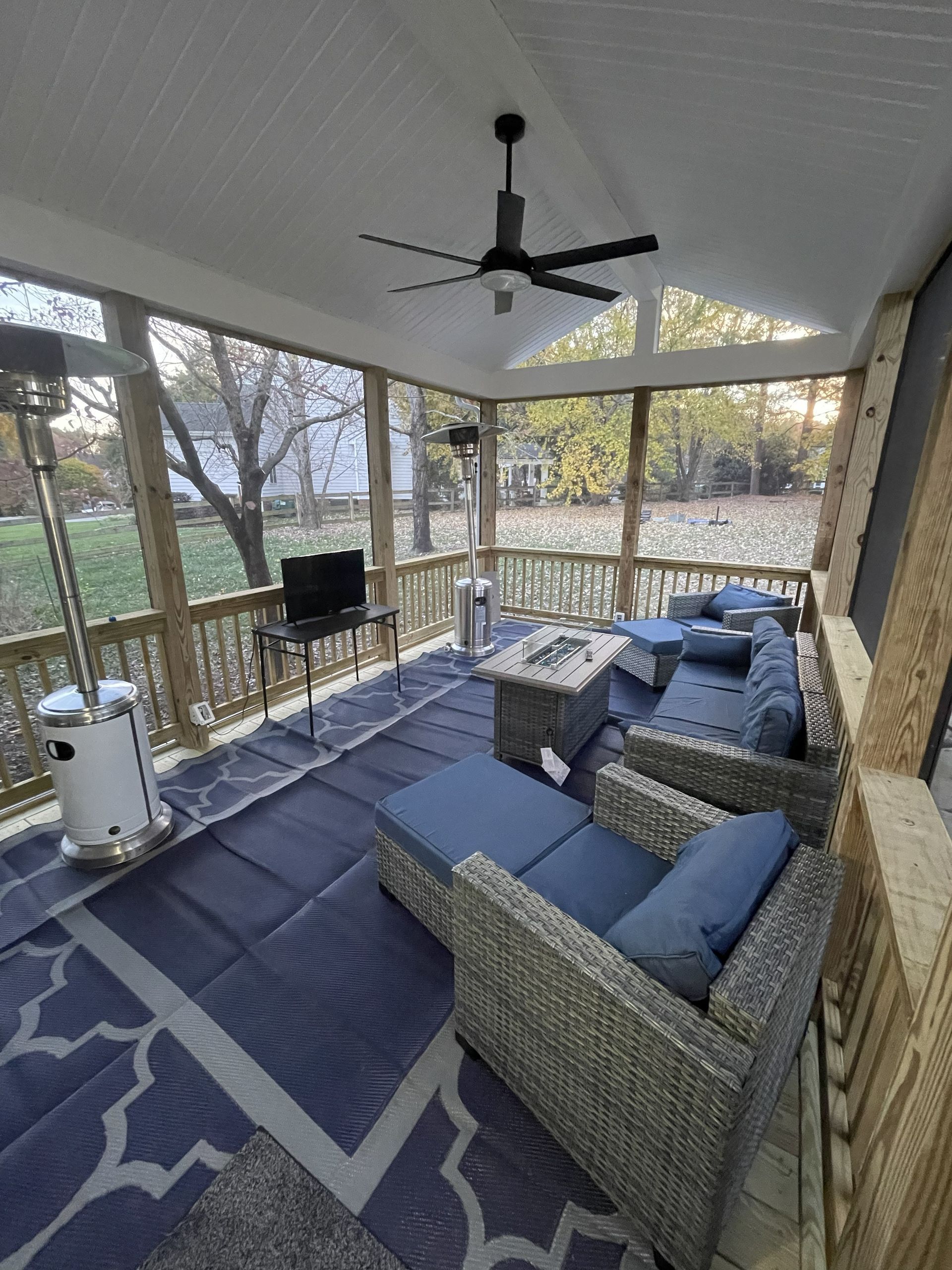 Covered porch with wicker seating, blue cushions, rug, ceiling fan, and grill overlooking trees