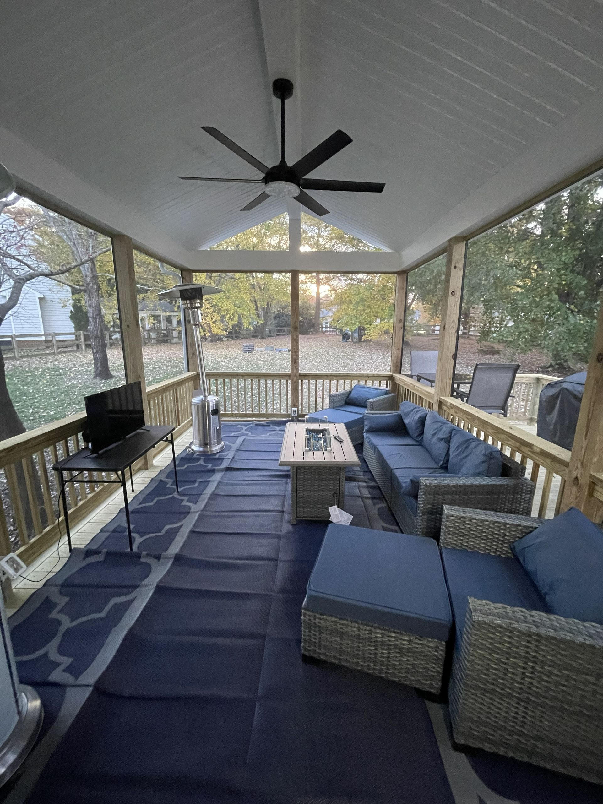 Covered porch with blue sectional seating, ceiling fan, and patio table overlooking trees and yard