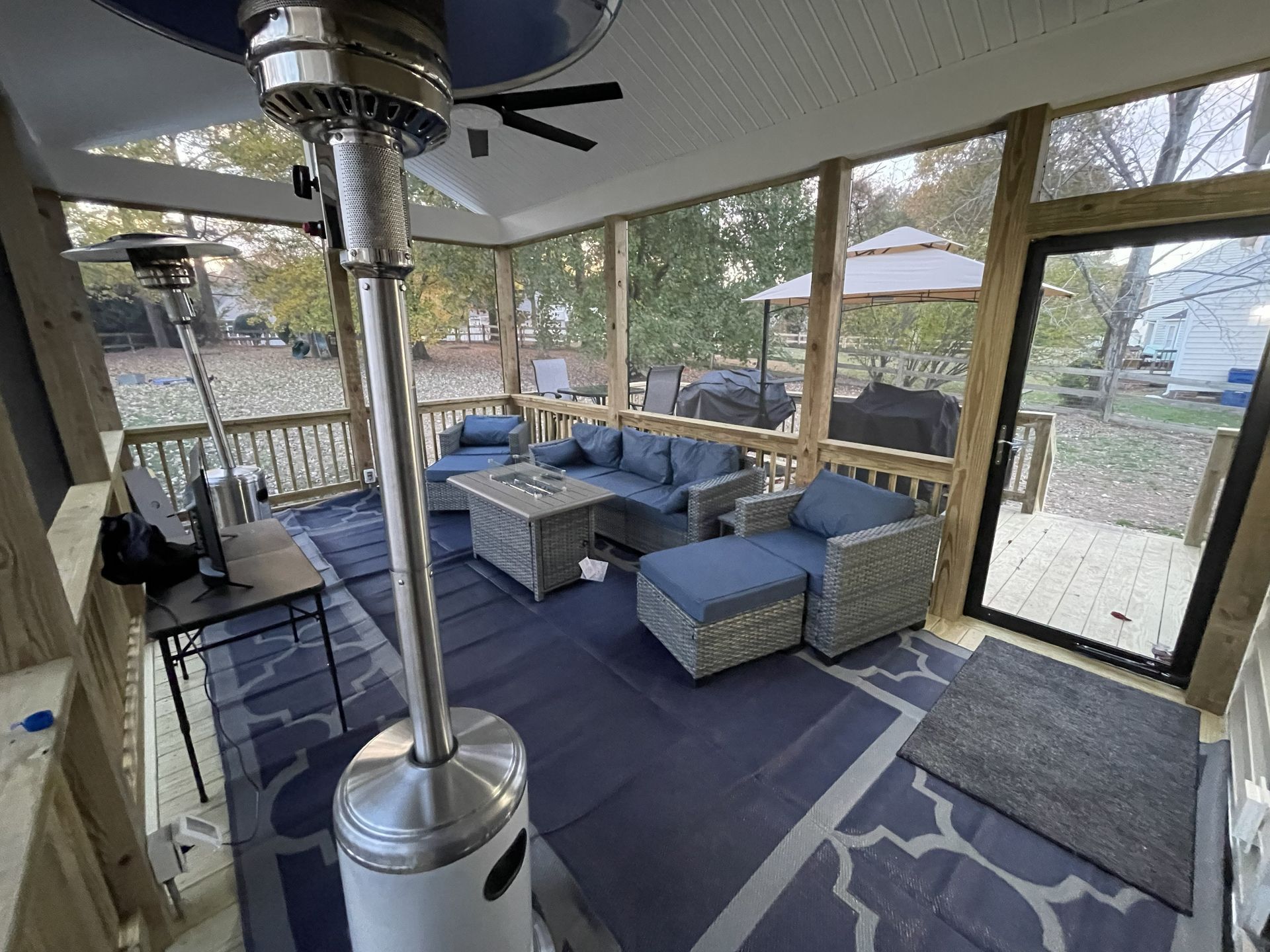 Covered outdoor patio with blue seating, rug, and patio heater, enclosed by screen walls and large windows