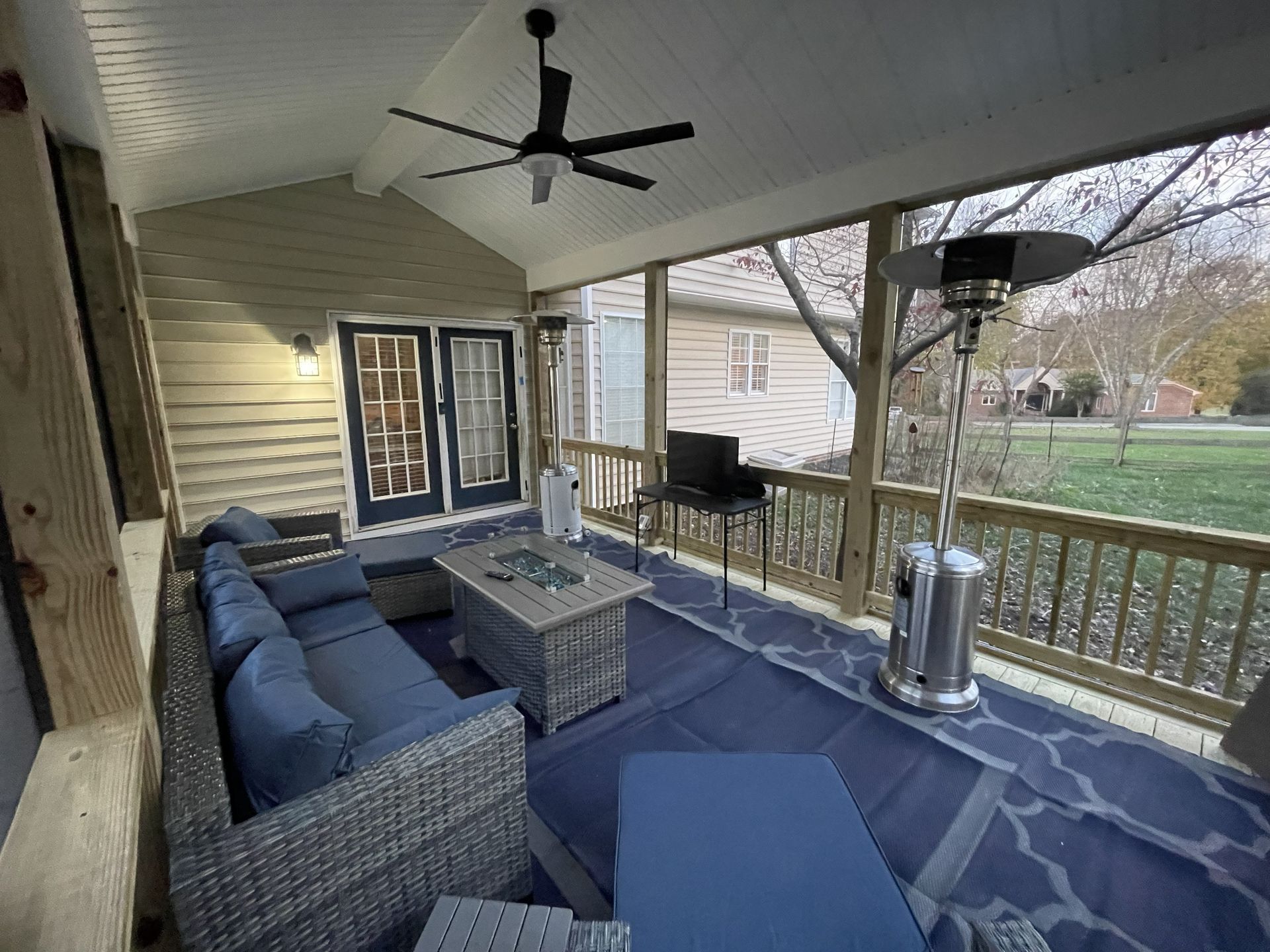 Covered porch with wicker sofa, blue cushions, coffee table, grill, and patio heater overlooking a yard