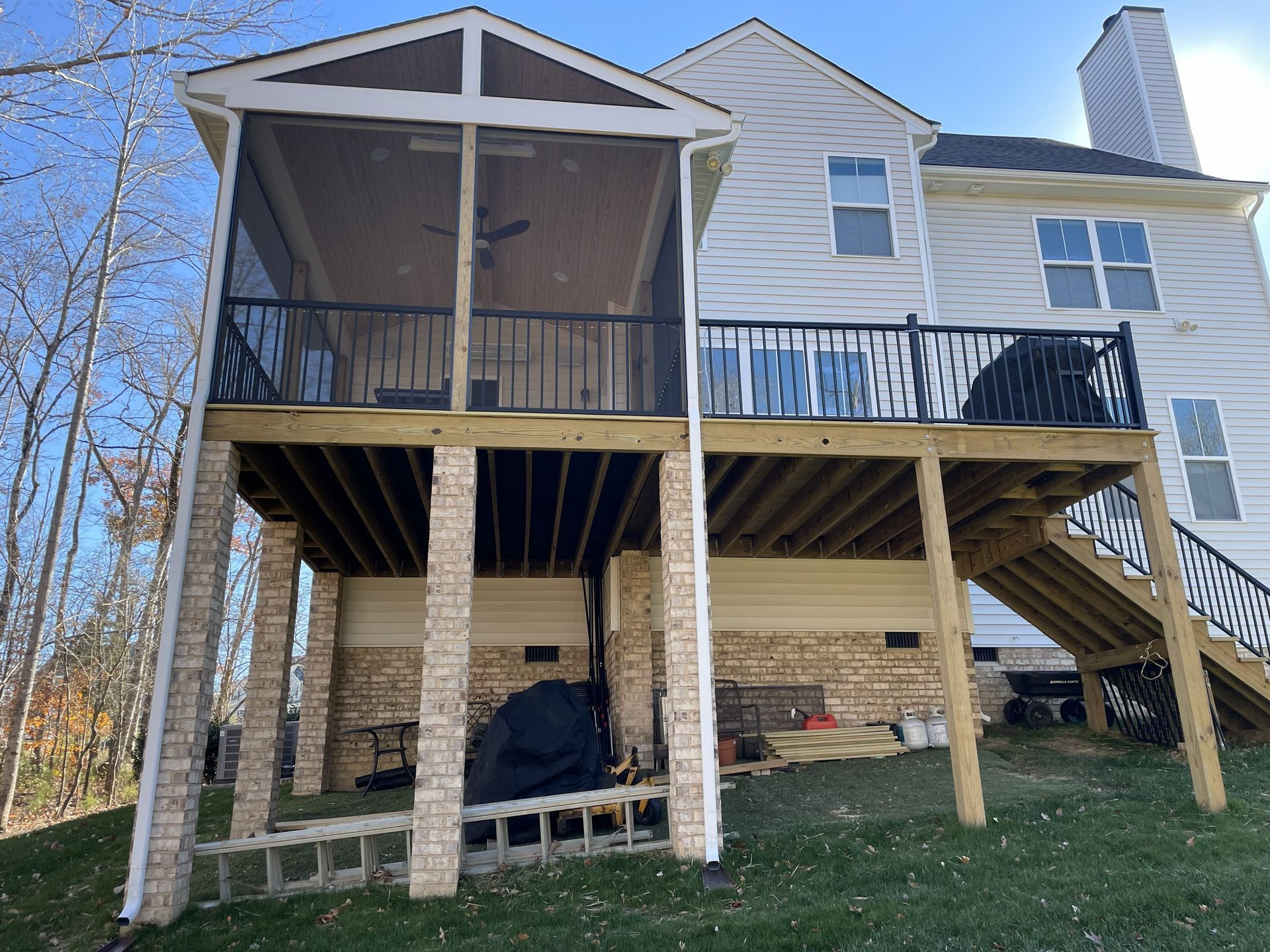 Two-story house with raised deck, screened porch, and exterior staircase on a grassy slope.