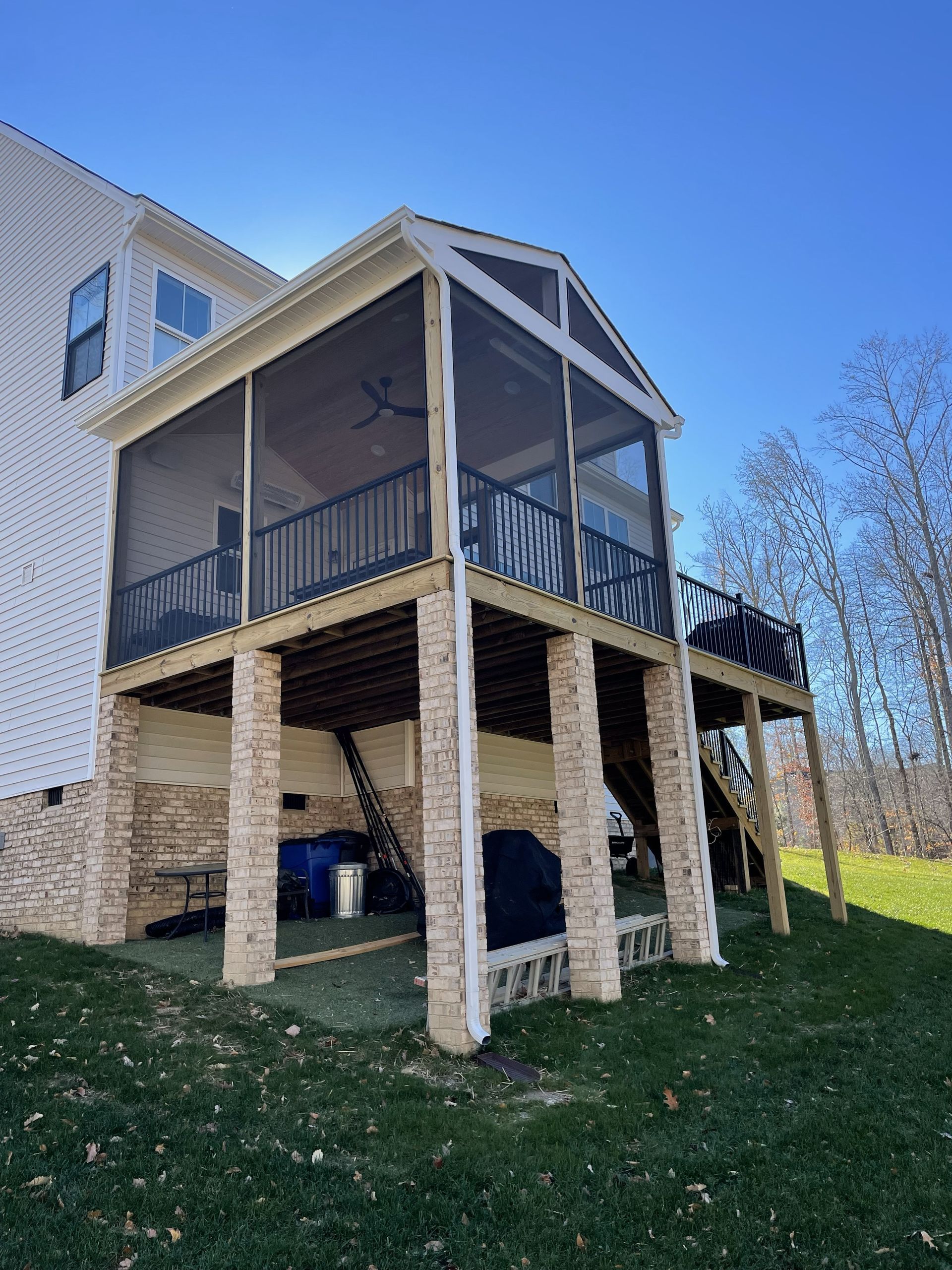 Elevated screened porch with stairs and stone columns beside a house on a grassy slope
