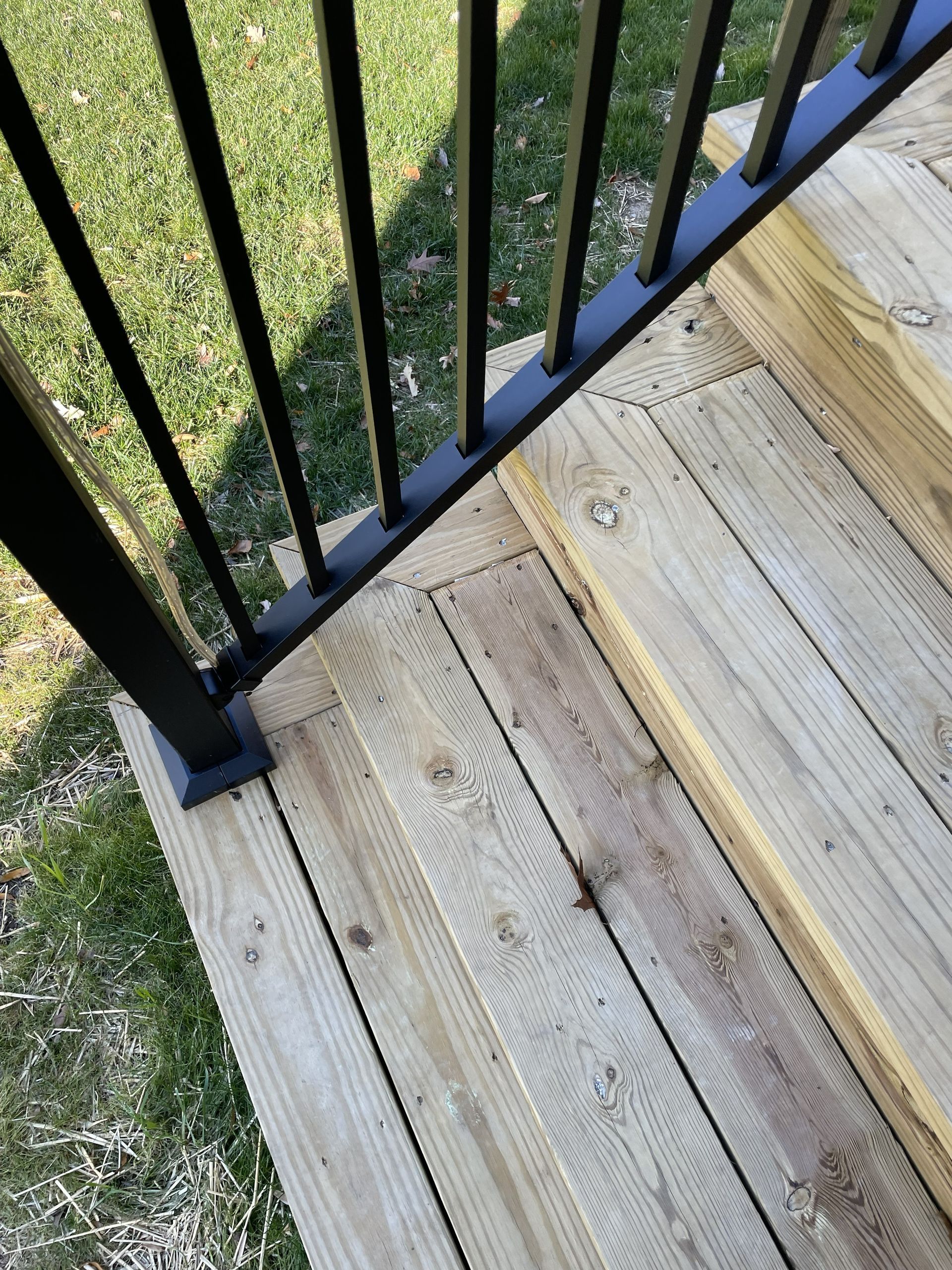 Black metal railing beside weathered wooden deck boards and grass below