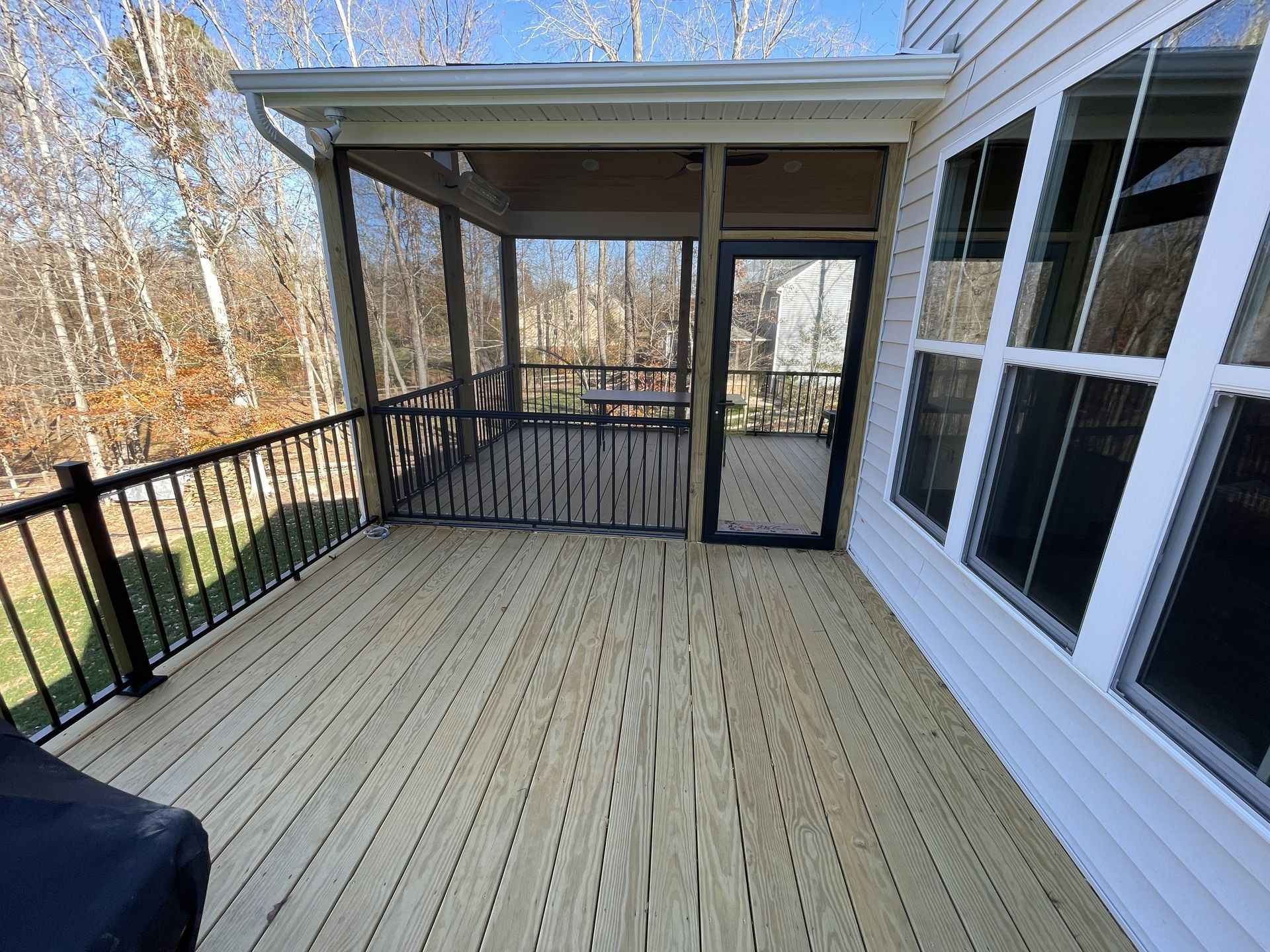 Covered wooden deck with black railing and screened porch beside a house