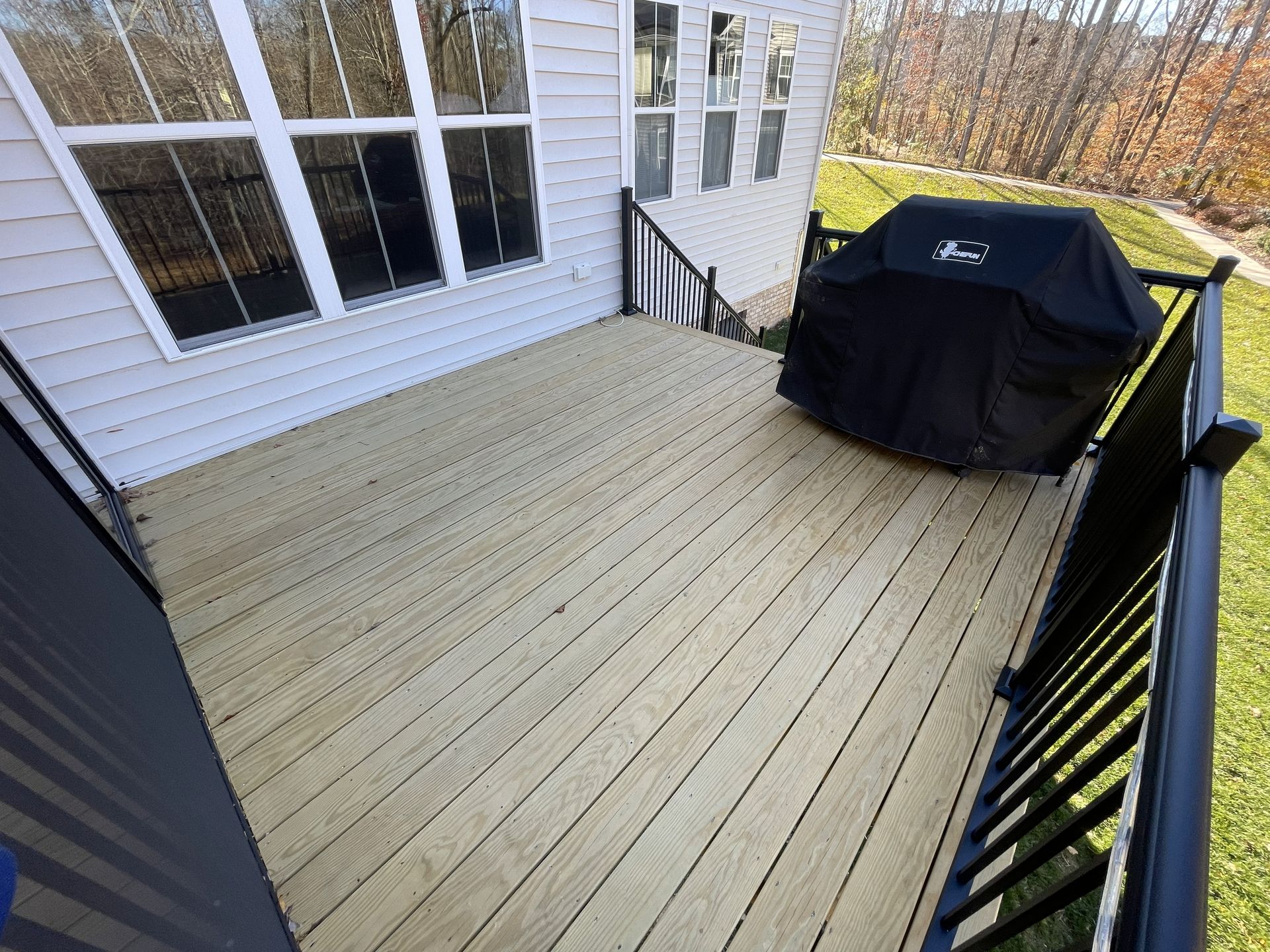 Wooden deck with black railing, sliding glass doors, and a covered grill beside the house.