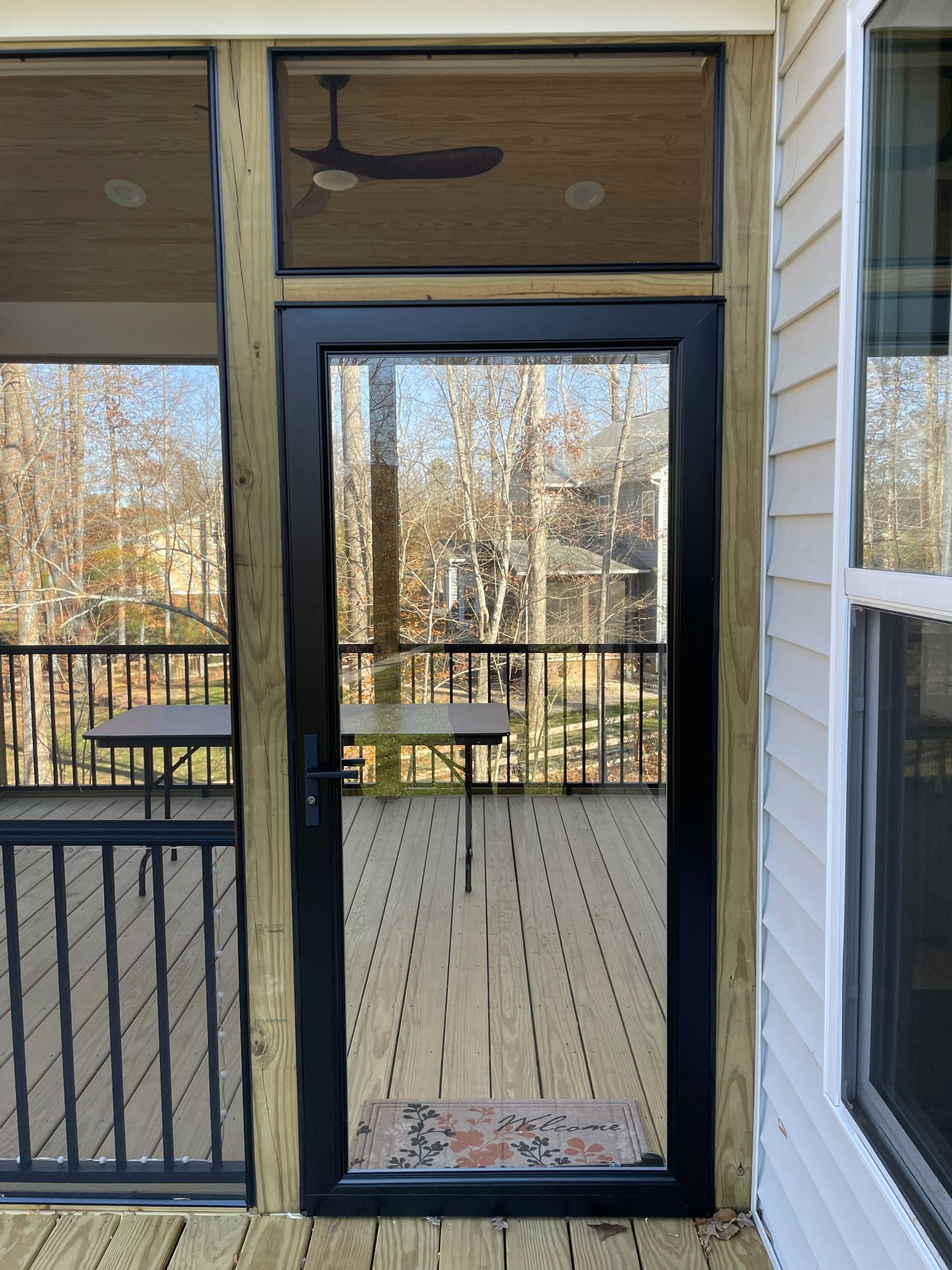 Screened porch door with black frame, overlooking a deck and wooded yard.