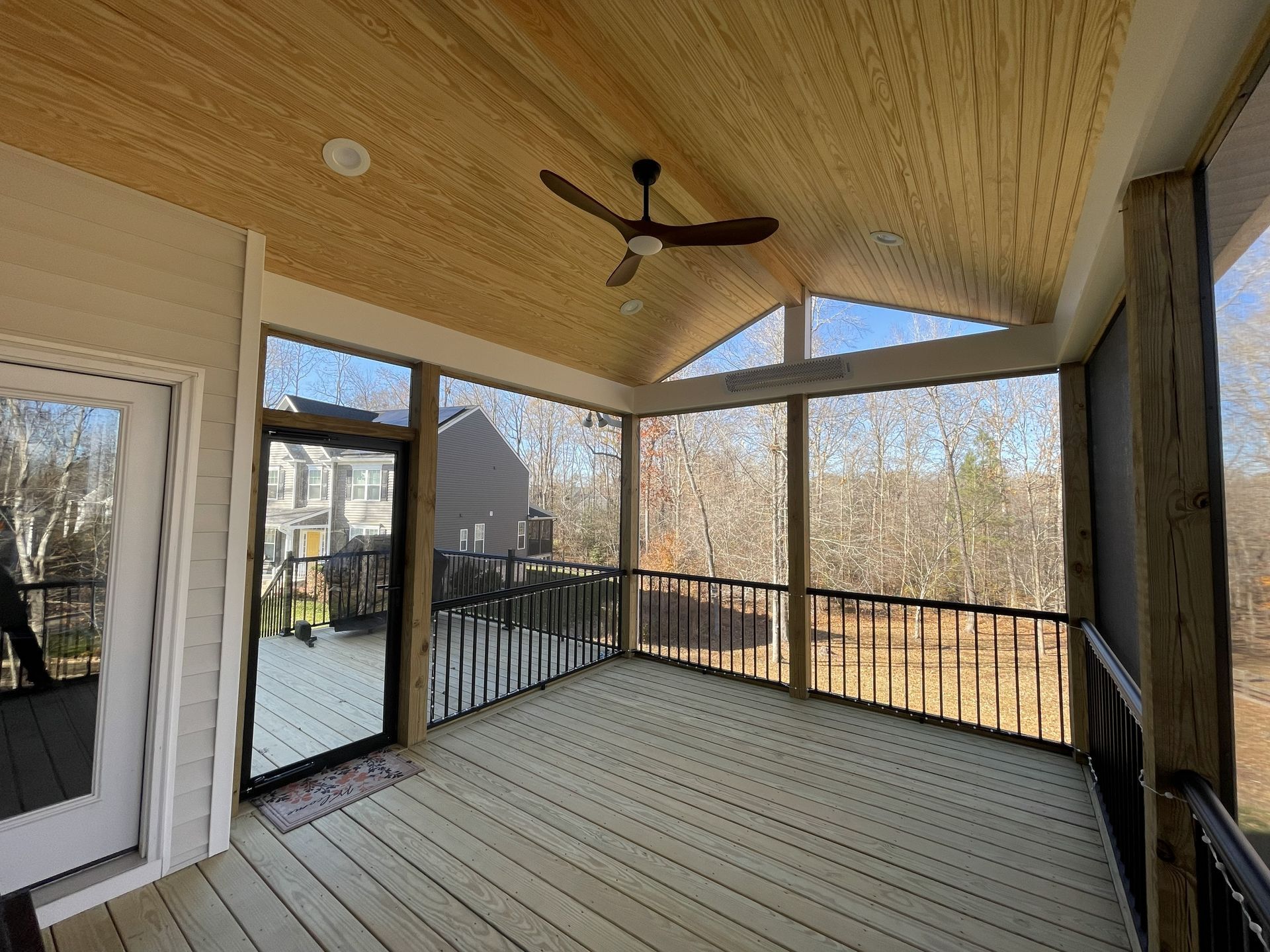 Covered wooden porch with ceiling fan, black railing, and view of a snowy backyard