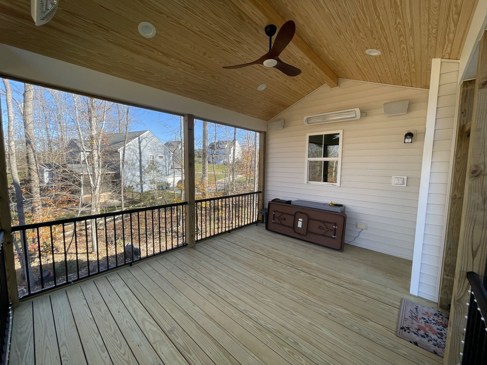 Covered wooden porch with railing, ceiling fan, and storage chest overlooking trees and a yard