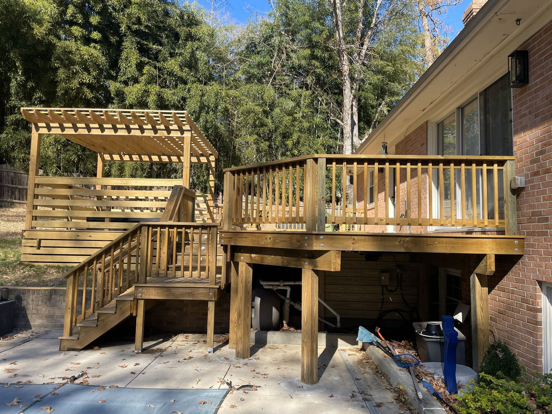 Wooden backyard deck with pergola beside a house, set among trees in sunlight