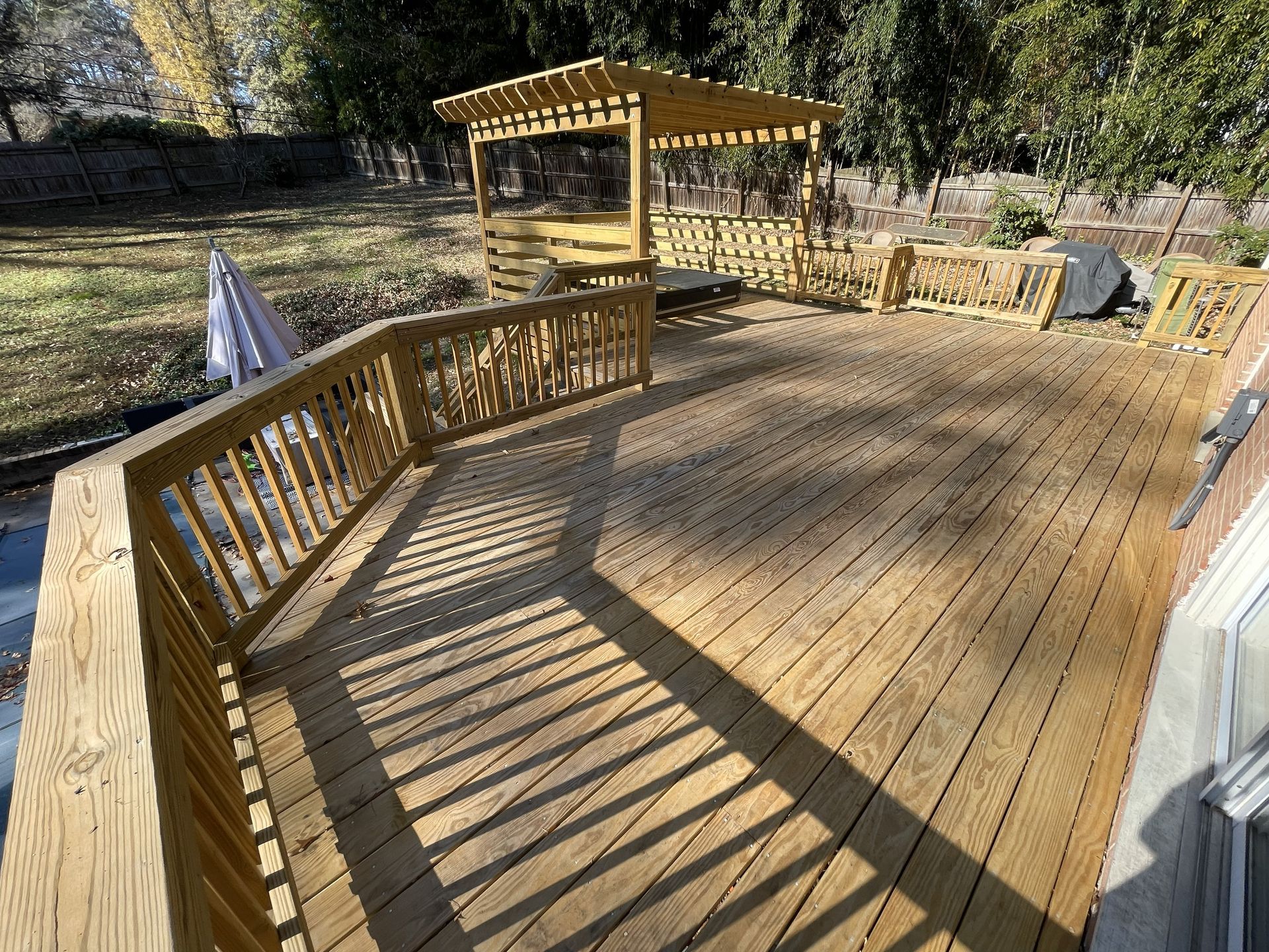 Wooden deck with railings and a small gazebo in a sunny backyard