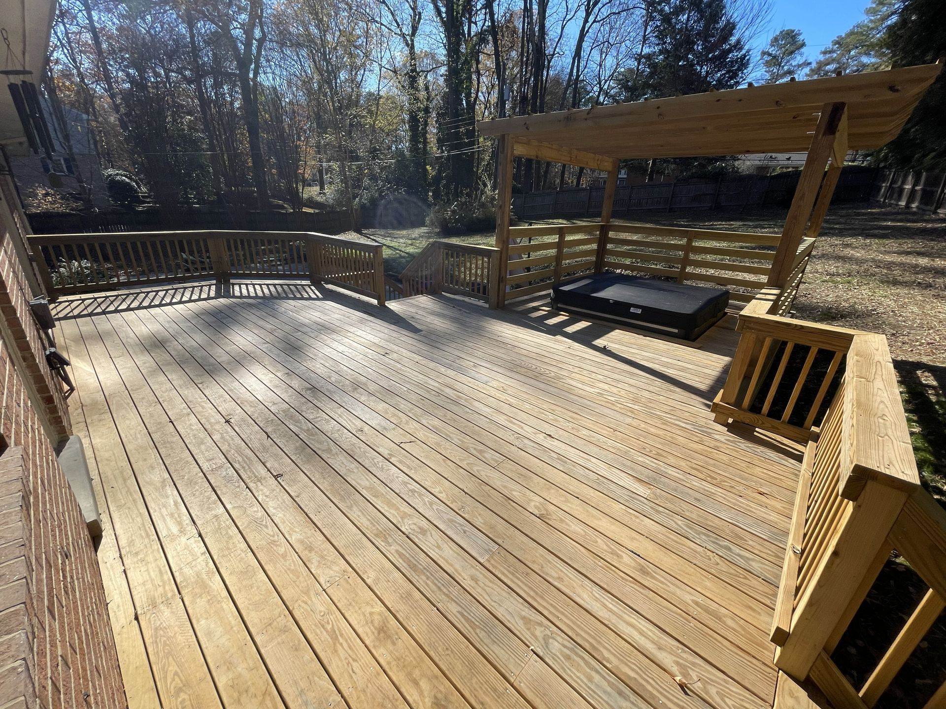 Wooden backyard deck with railings and a pergola, surrounded by trees in sunlight
