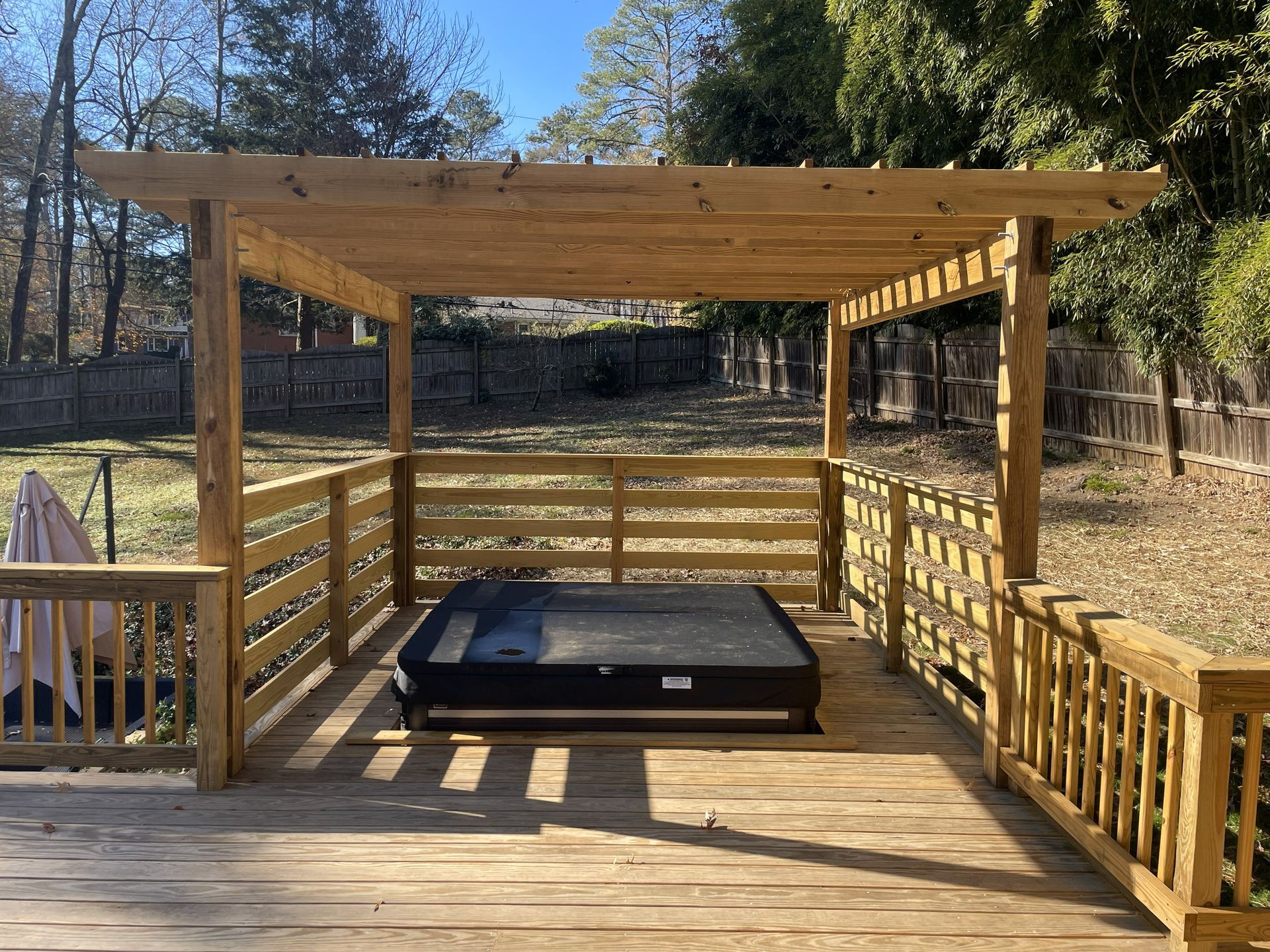 Wooden deck pavilion with railings and a black hot tub in a wooded backyard