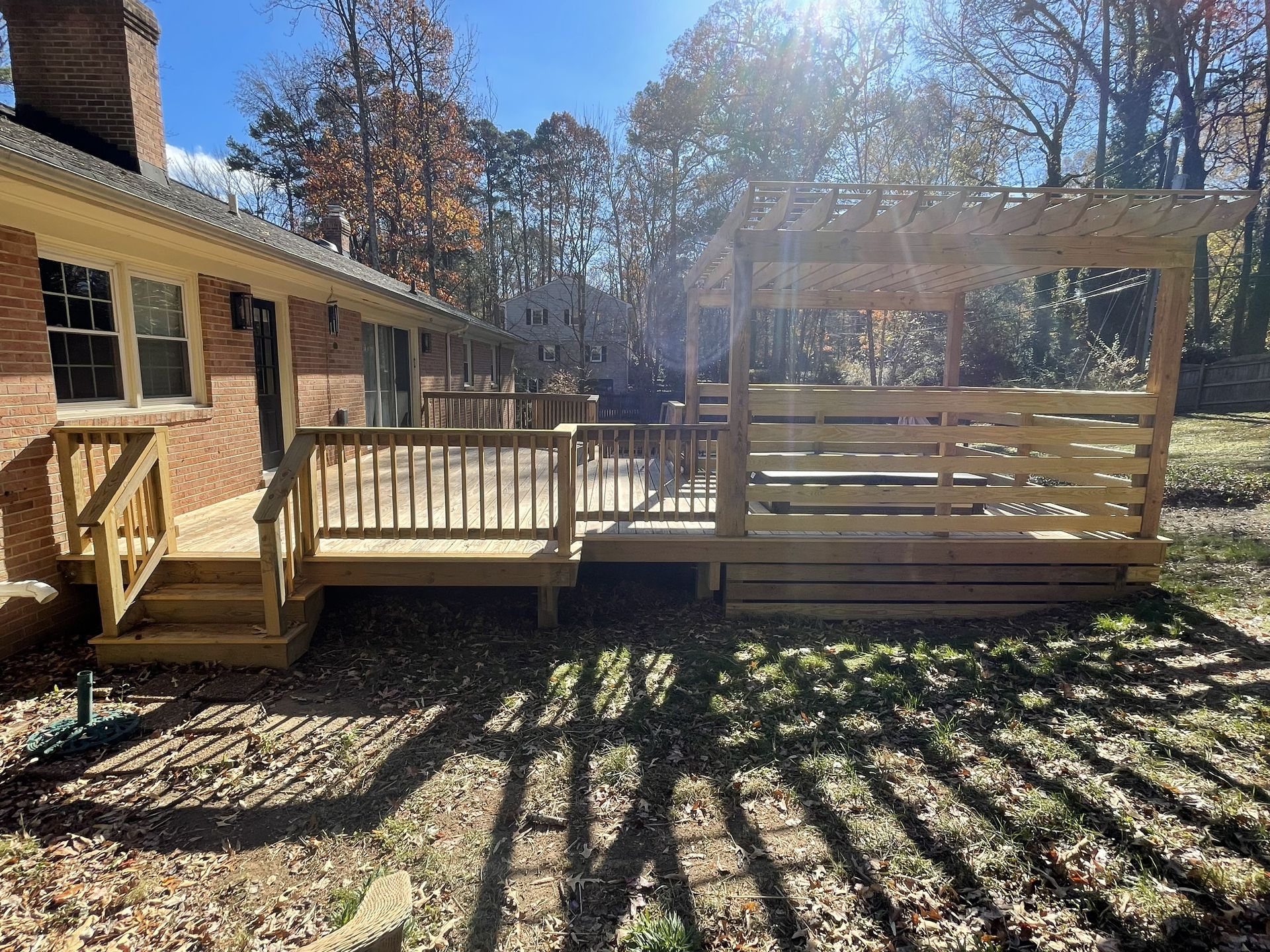 Wooden deck with railing beside a house, overlooking a sunny backyard with long shadows.