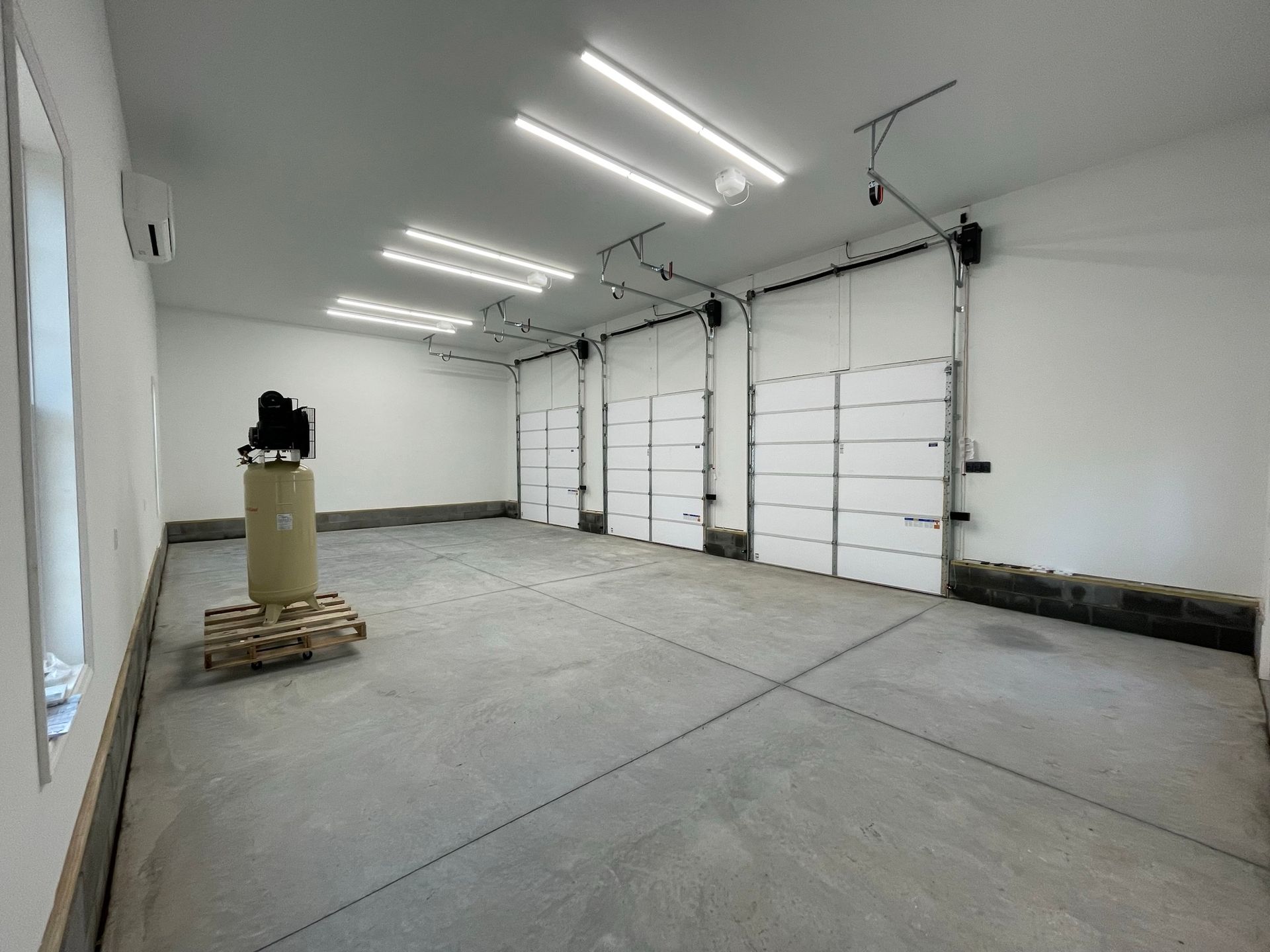 Empty garage interior with white overhead doors, concrete floor, and fluorescent lights