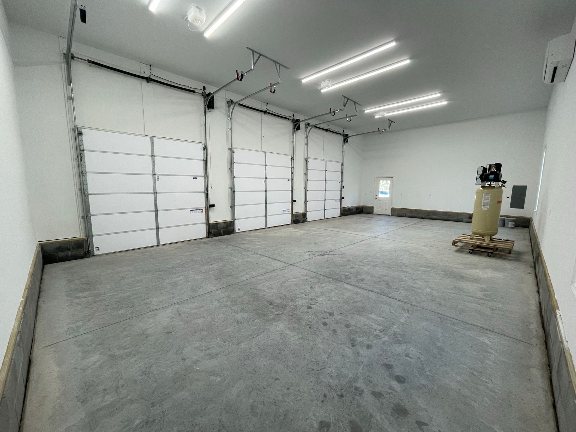 Empty garage interior with concrete floor, white overhead doors, and fluorescent lights