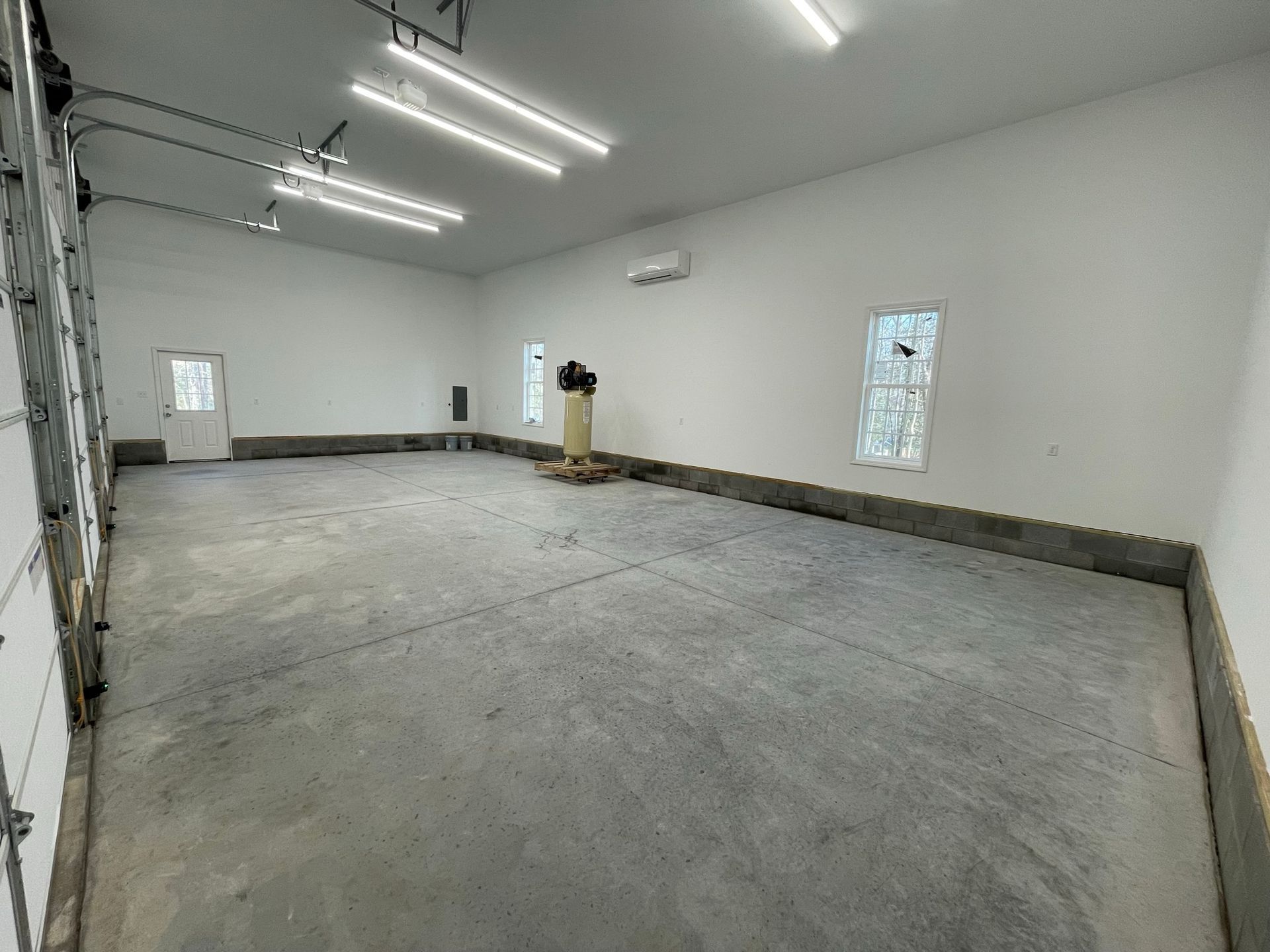Empty concrete garage or workshop with white walls and overhead fluorescent lights
