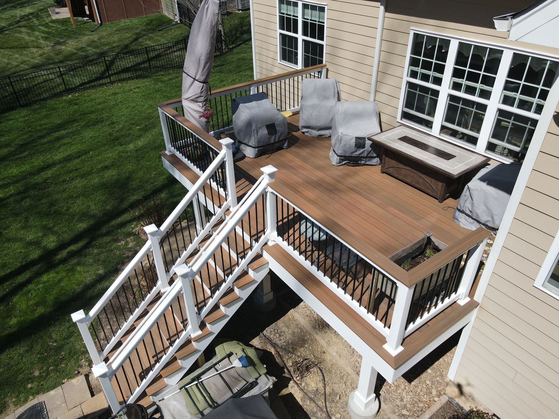 Wooden deck with white railings, outdoor chairs, and a grill beside a house, viewed from above