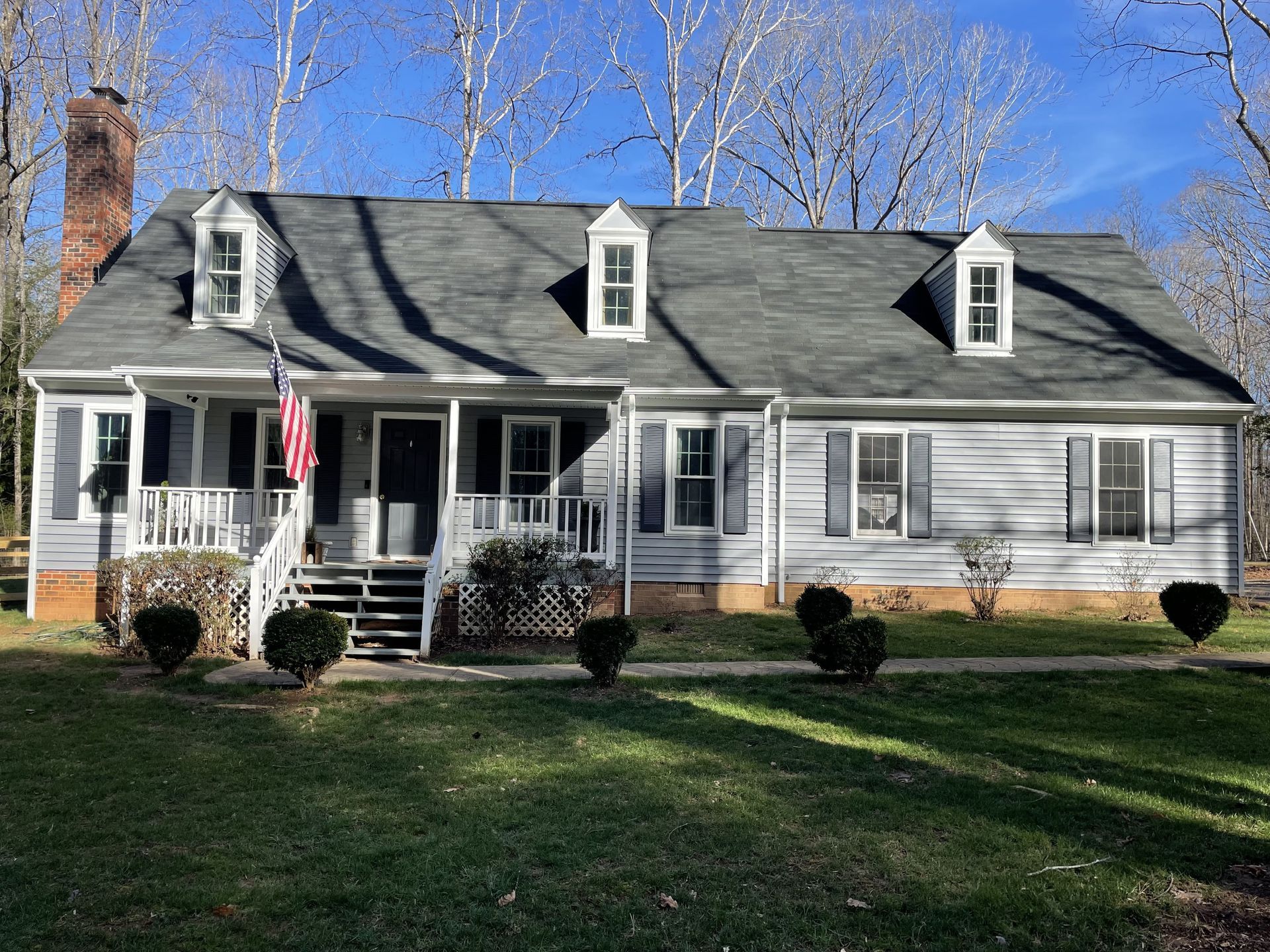 White house with black roof, front porch, and American flag in a sunny yard
