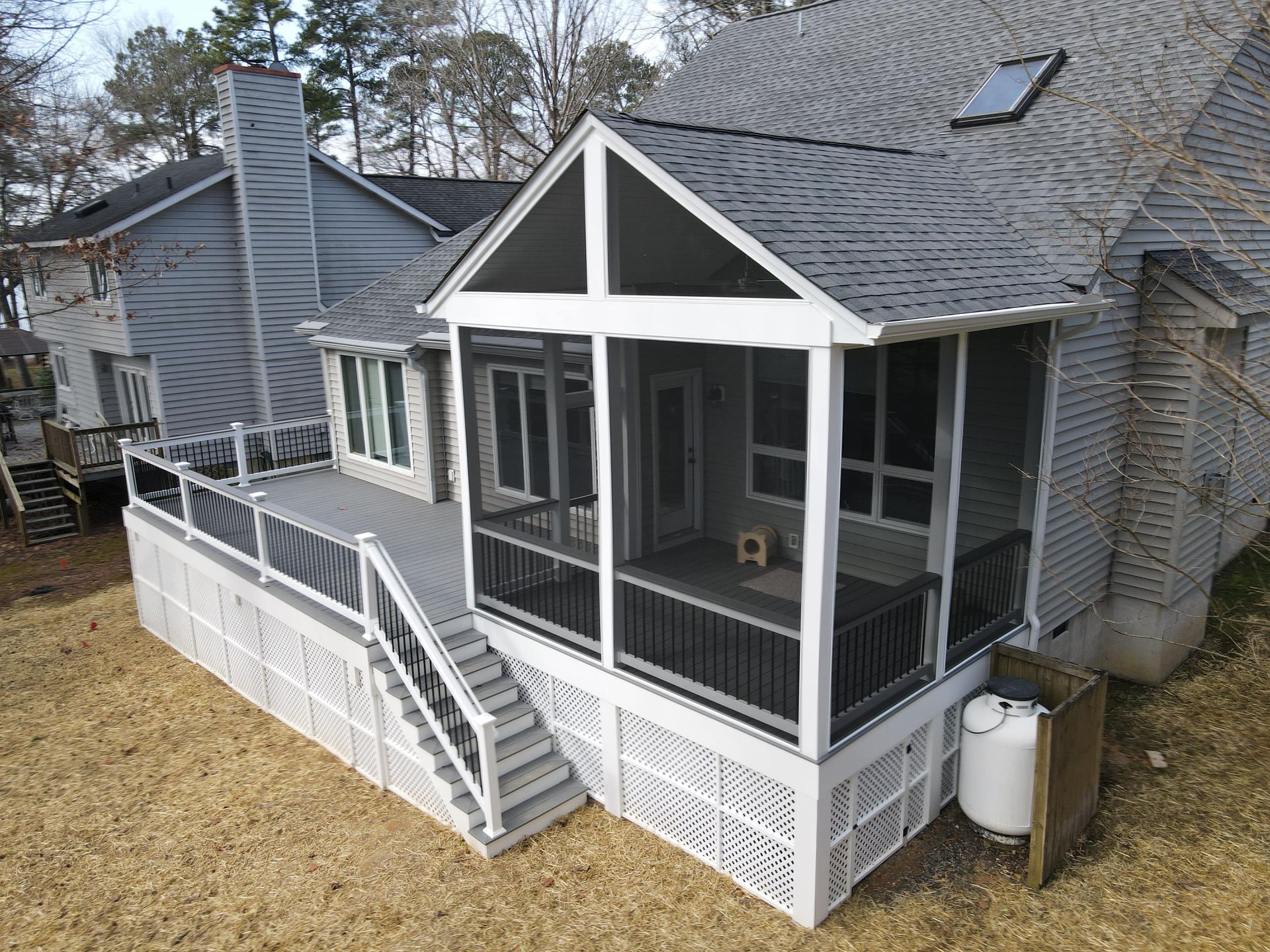 Rear view of a house with a screened-in porch, white railings, and a staircase leading down to the yard