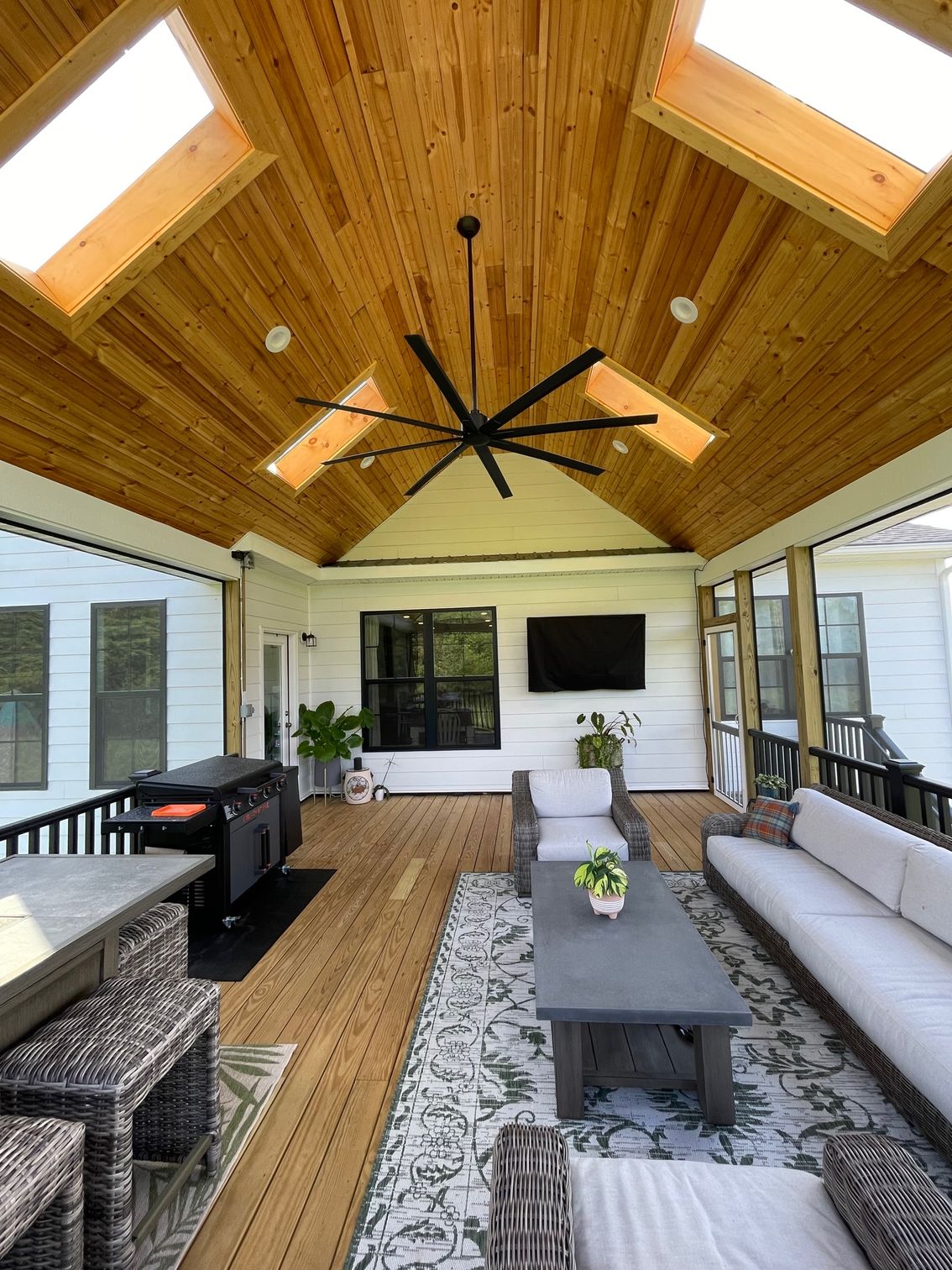 Covered patio with wood ceiling, skylights, black fan, and outdoor seating around a coffee table.