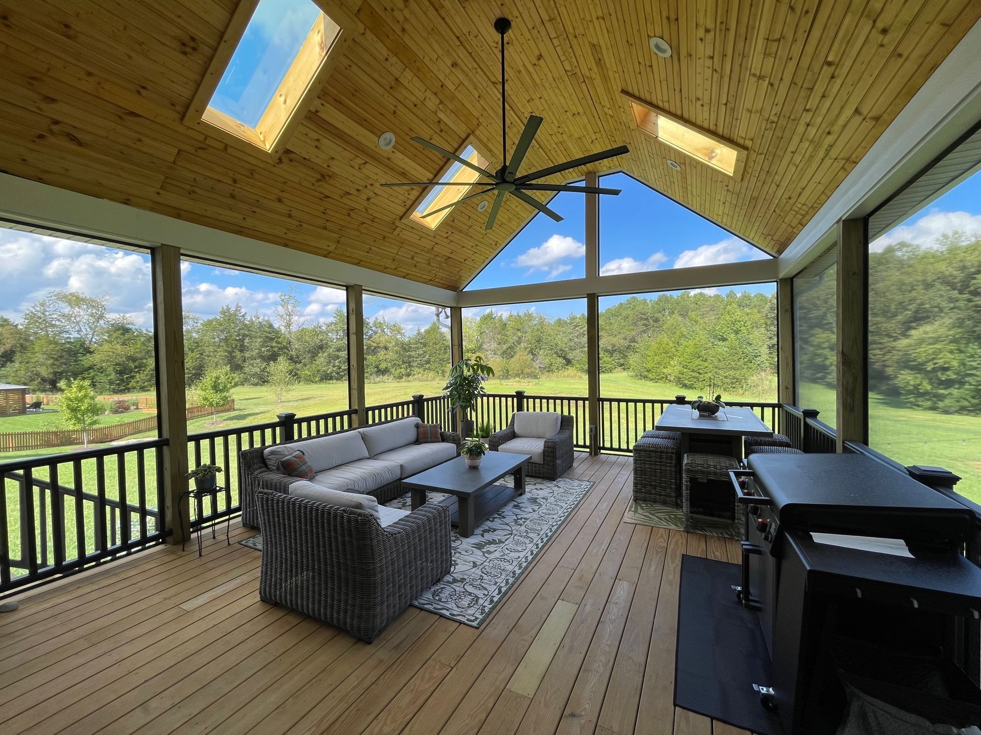 Covered screened porch with wicker seating, dining table, and outdoor grill overlooking a green yard.