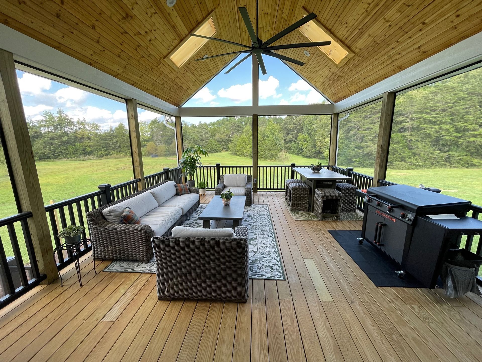 Covered outdoor patio with wicker seating, grill, and open view of a grassy yard