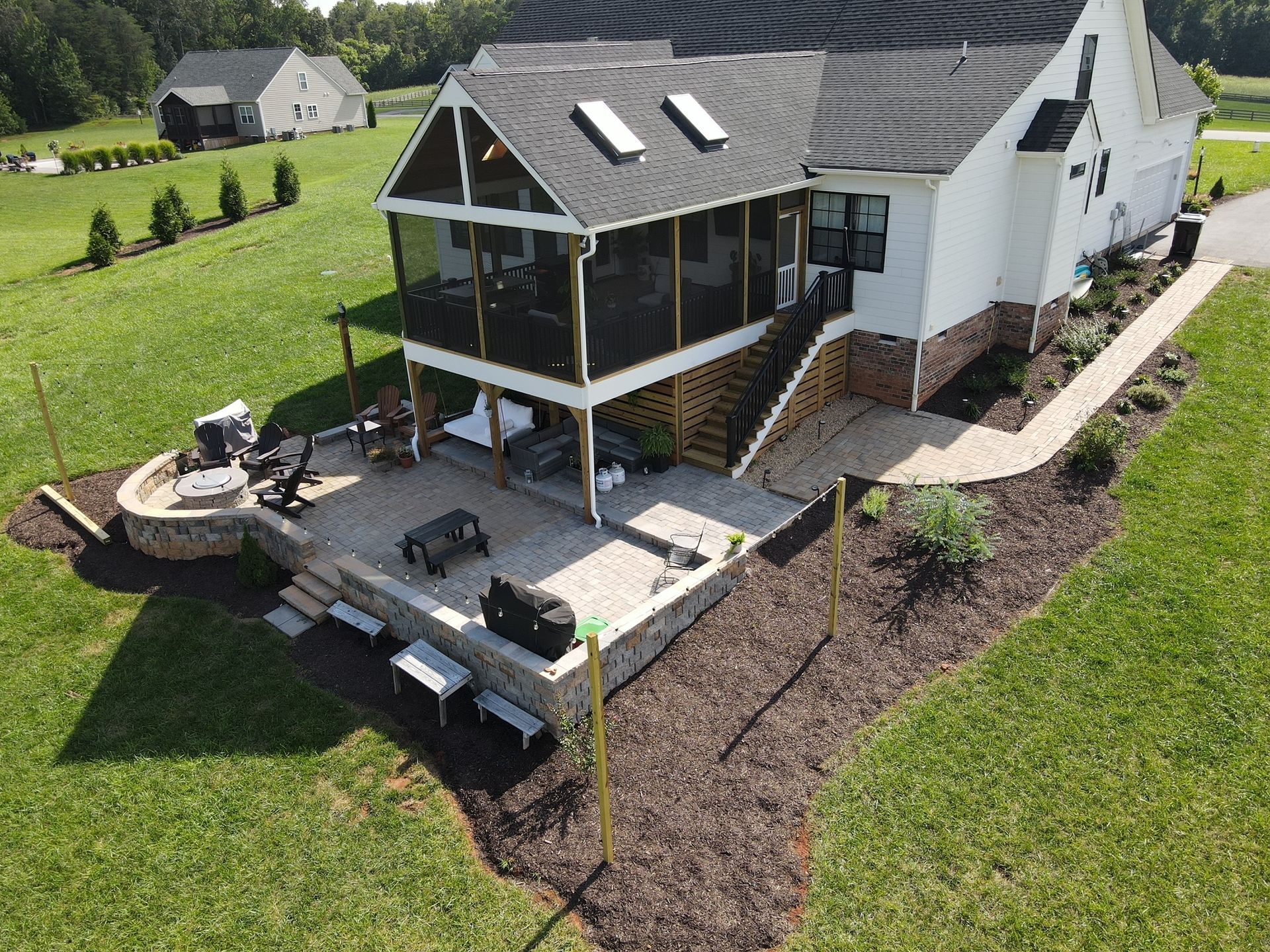 Aerial view of a house with a covered deck, patio furniture, and a landscaped backyard.